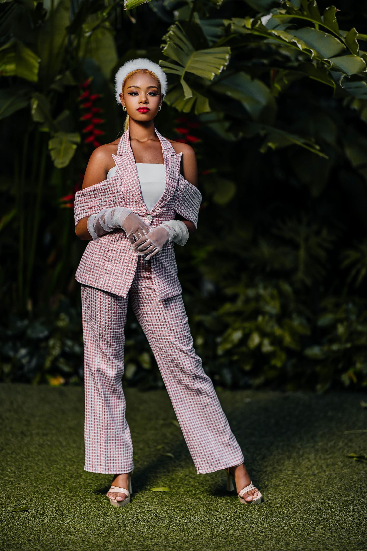 Chic pink gingham pantsuit with off-shoulder styling against green garden background.