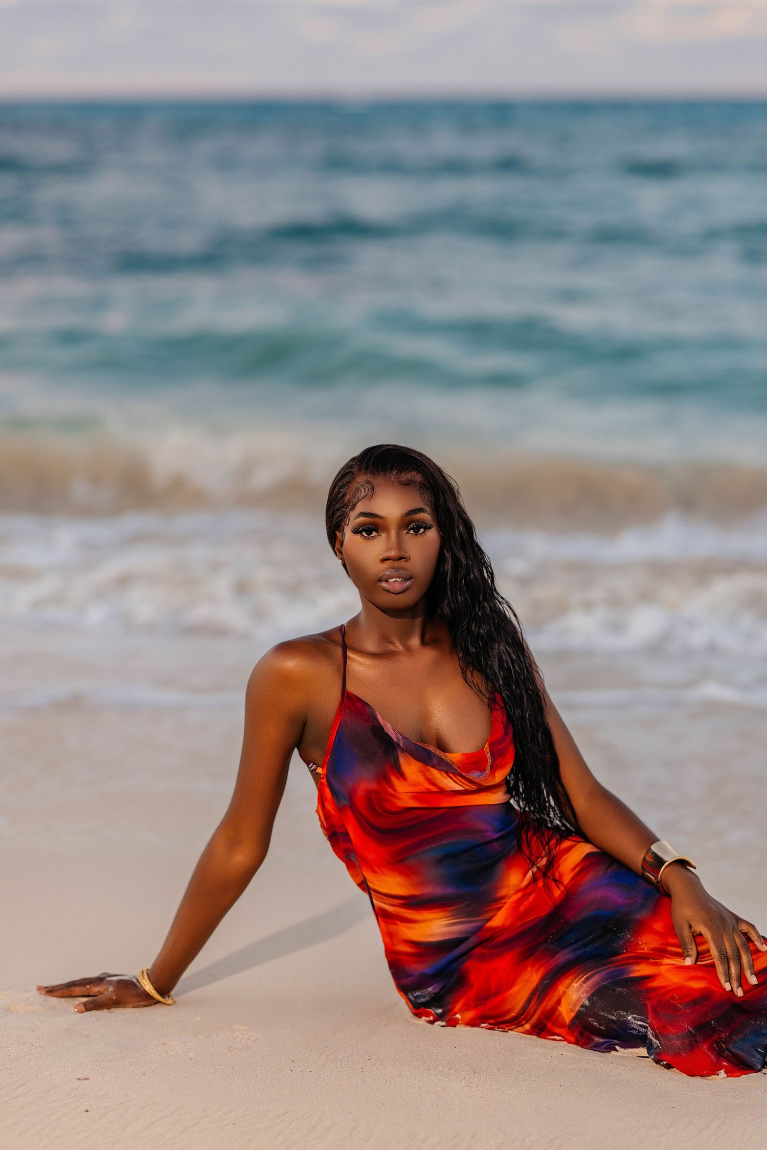 Beach fashion shoot featuring model in flowing red and navy dress on sandy shore.