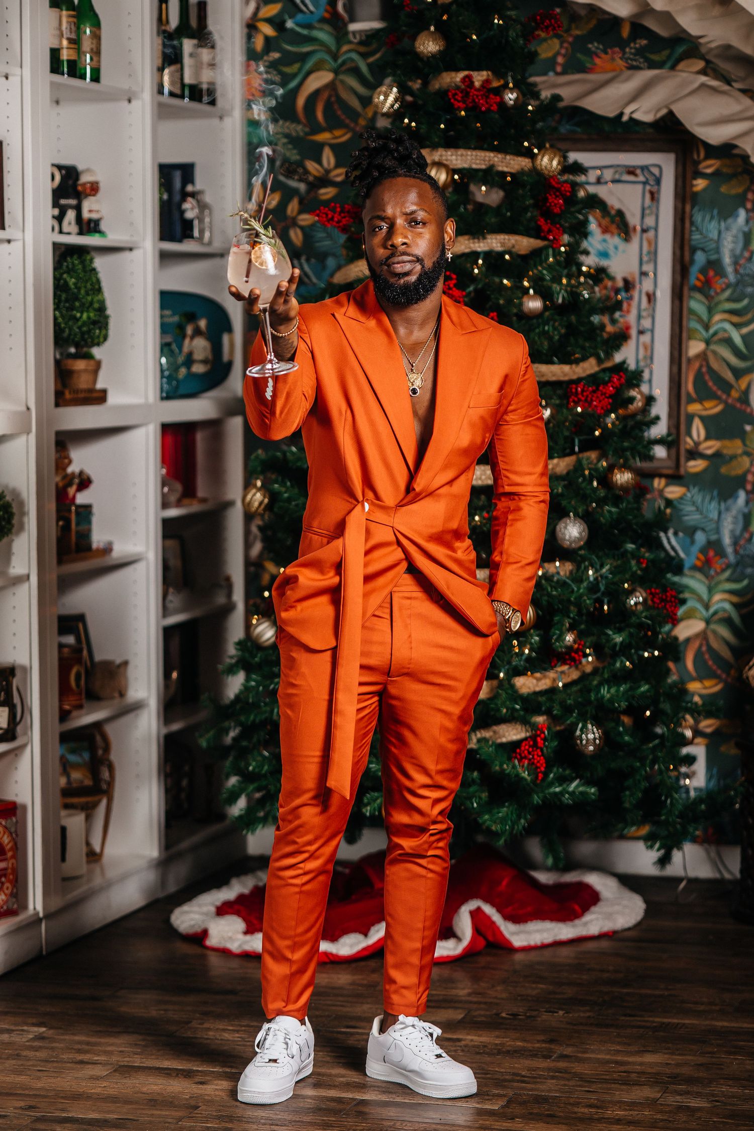 Bright orange fitted suit paired with white sneakers in front of decorated Christmas tree.