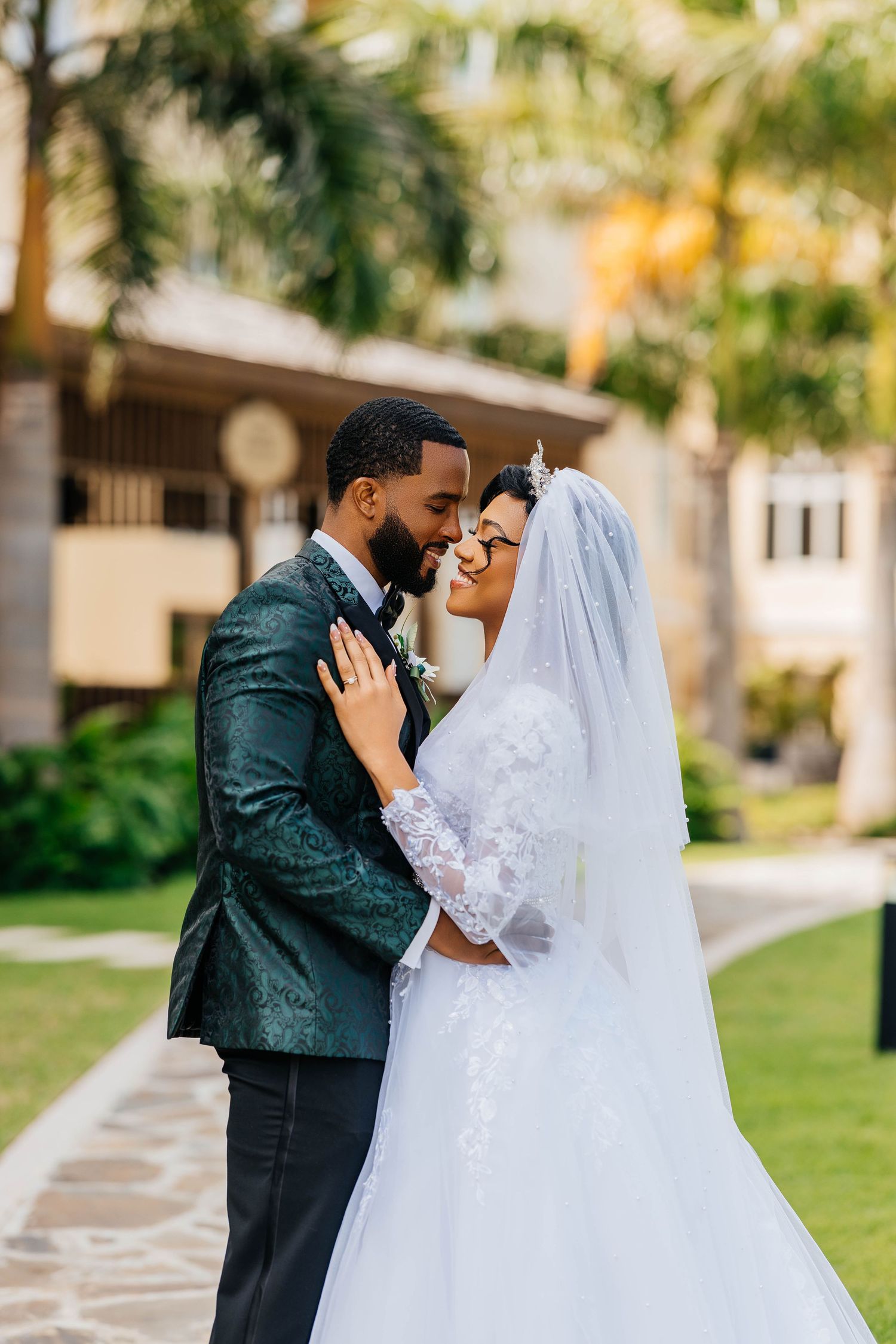 A romantic wedding moment captured outdoors with a couple in elegant attire embracing against a tropical garden backdrop.