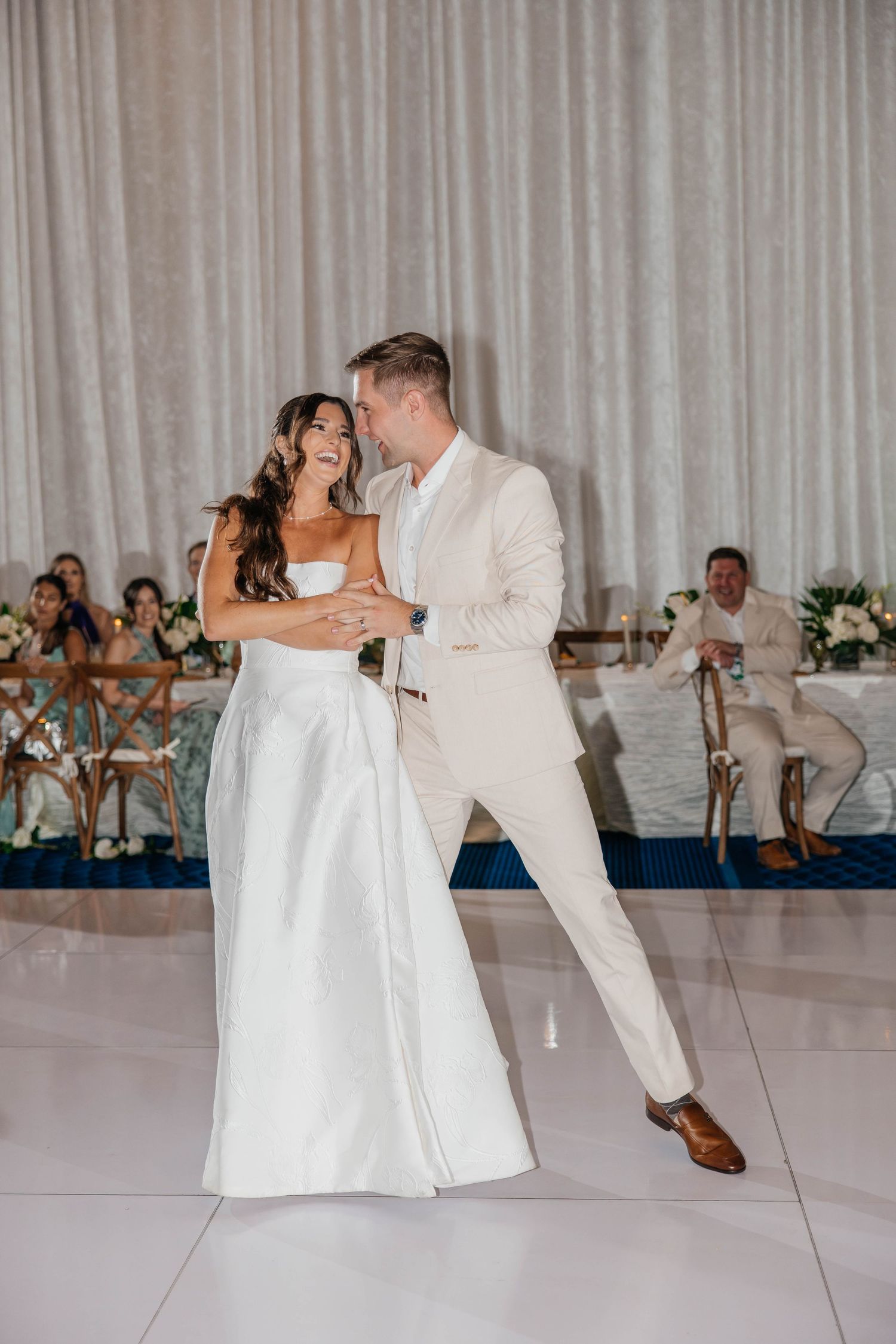 Bride and groom share their first dance on a white dance floor at an elegant wedding reception.