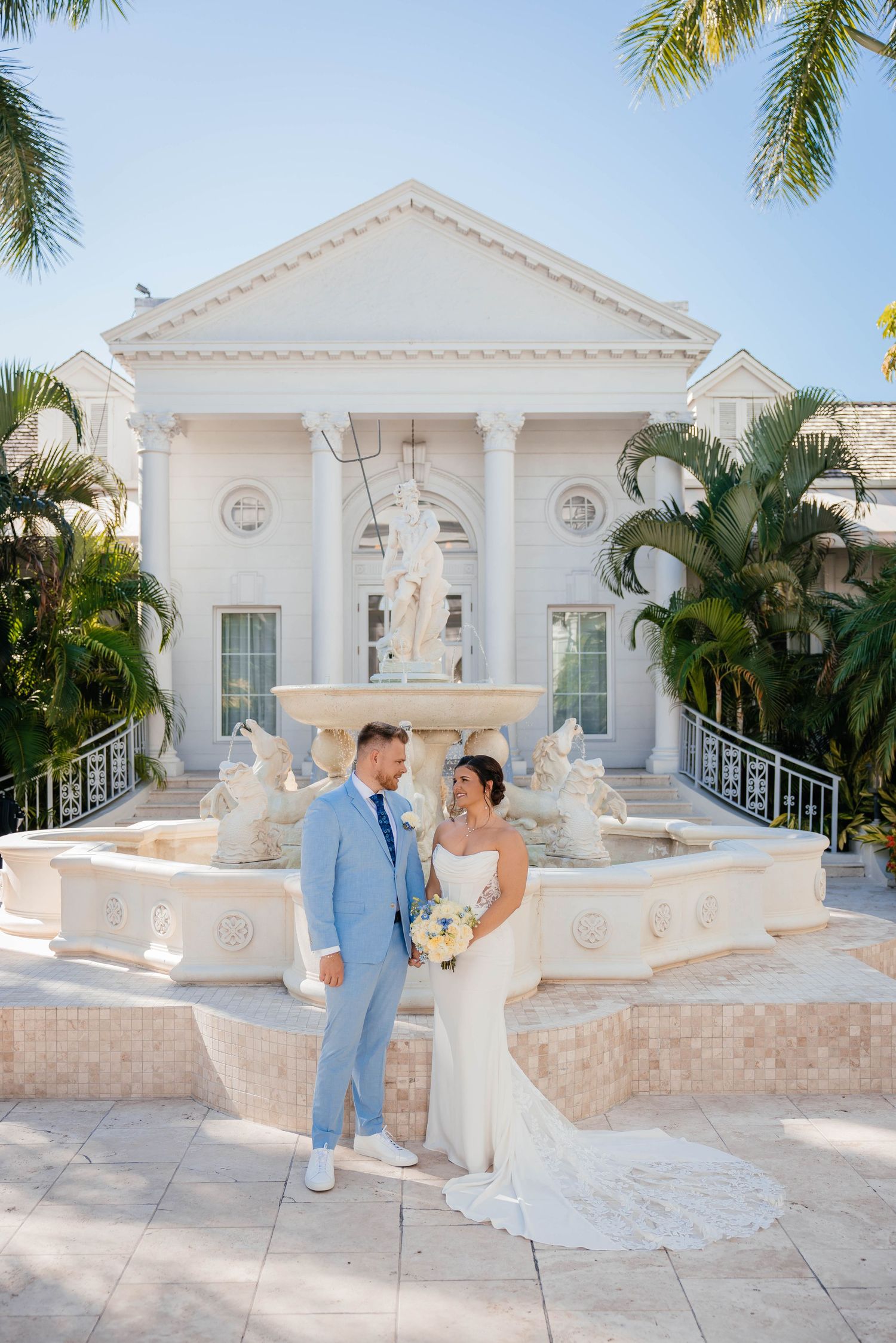 Elegant white wedding venue with palm trees and classic architecture features multiple romantic photo opportunities.