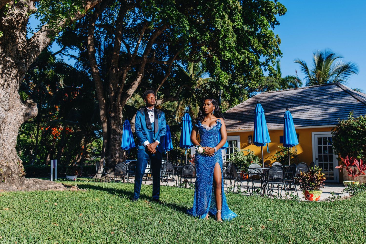 Group of people in blue dresses standing on a lawn next to a building with palm trees in the background.