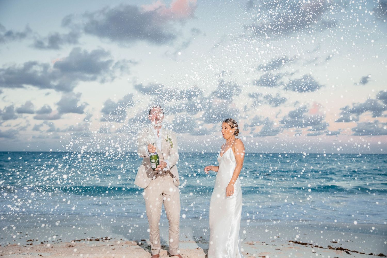 Wedding couple getting splashed by ocean waves during beach photoshoot.