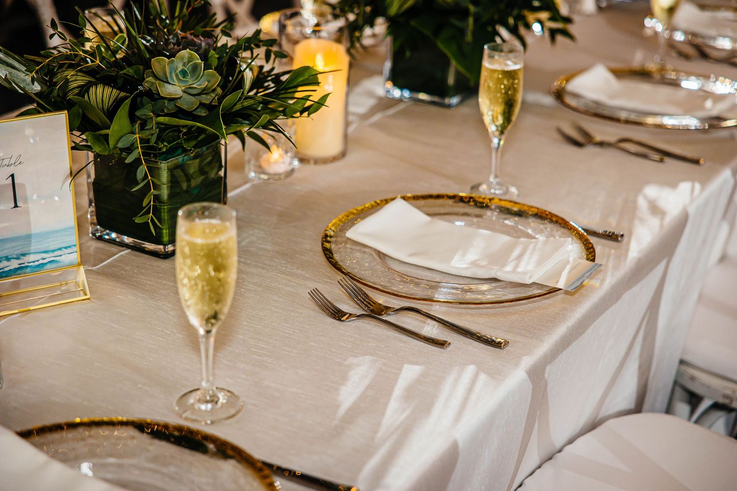 Luxurious wedding table setting with gold-rimmed charger plates, champagne flutes, and tropical floral centerpieces.