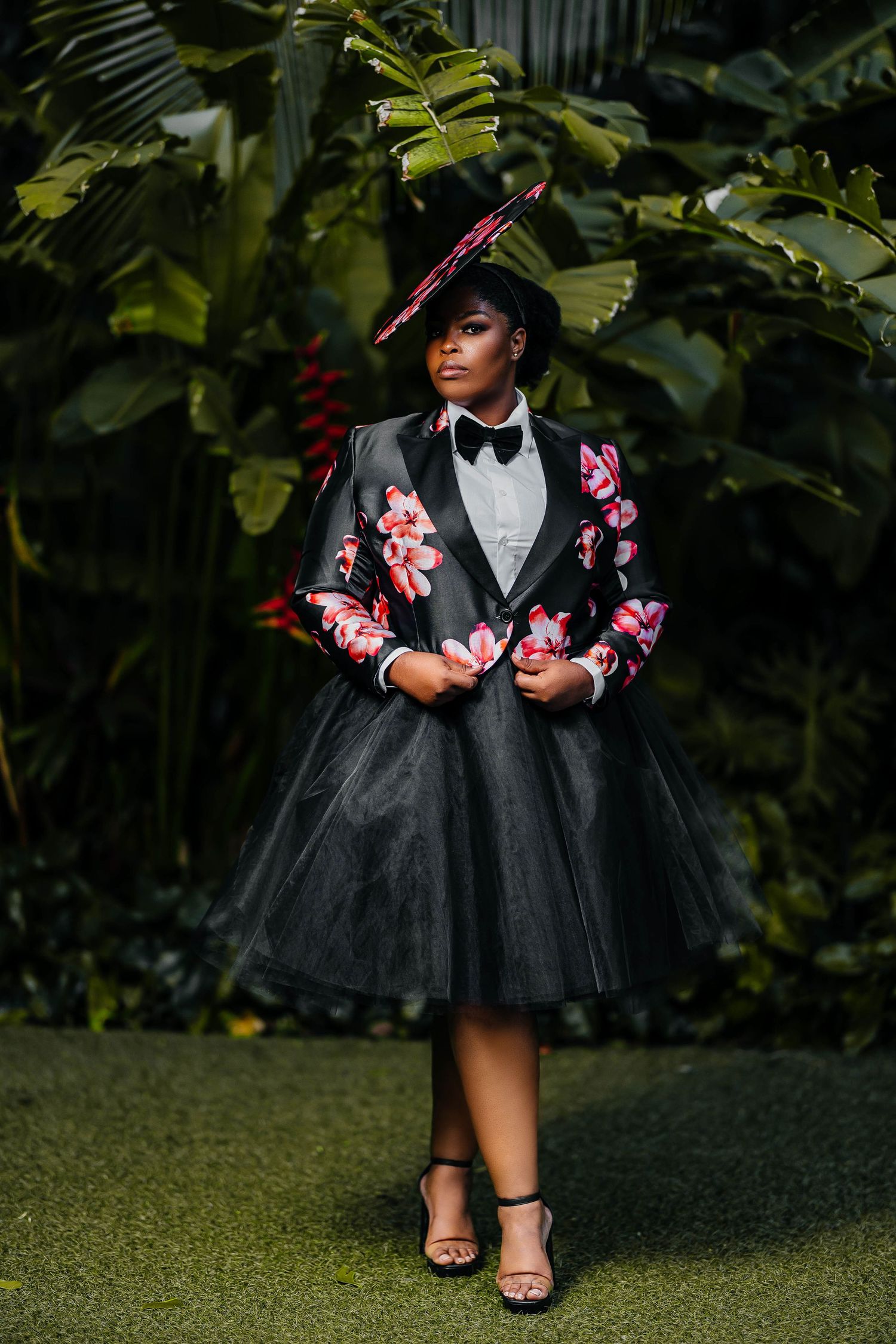 Formal portrait in black tulle dress and floral jacket against lush tropical backdrop.