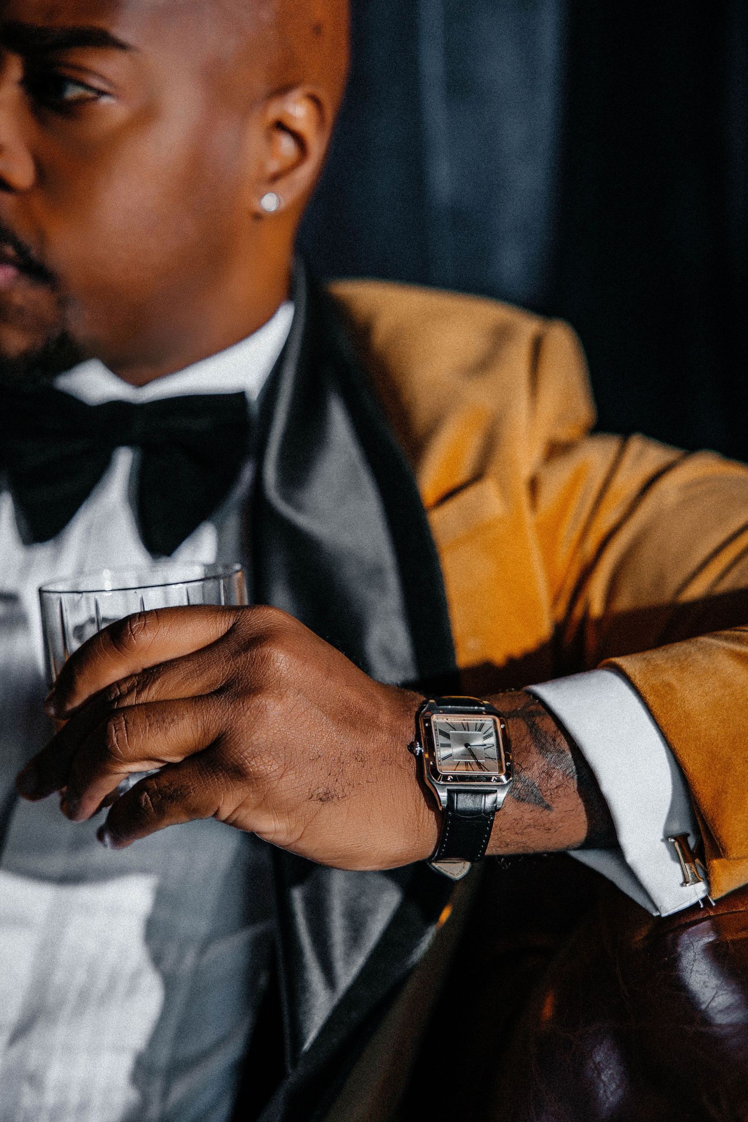 Close-up of man's hand with watch wearing gold tuxedo and black bow tie.