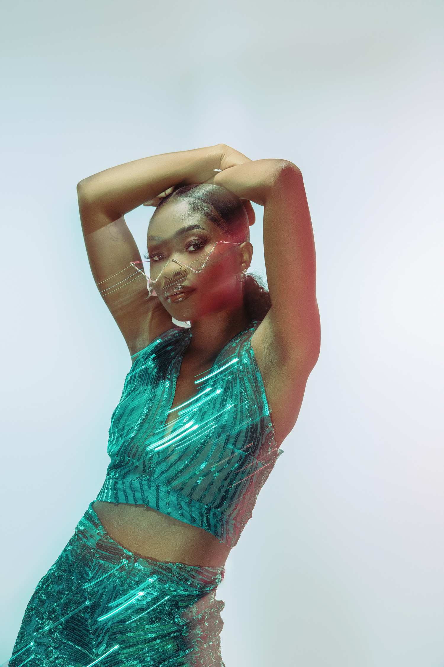 Artistic fashion photo of a model posing in shimmering turquoise outfit with dreamy lighting effects.
