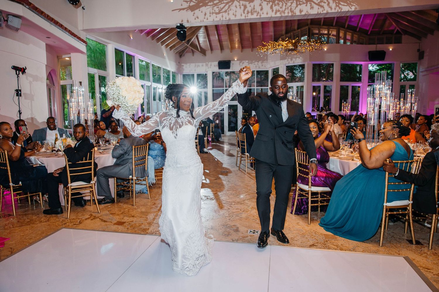 Bride and groom share first dance at elegant wedding reception with guests seated at decorated tables in background.