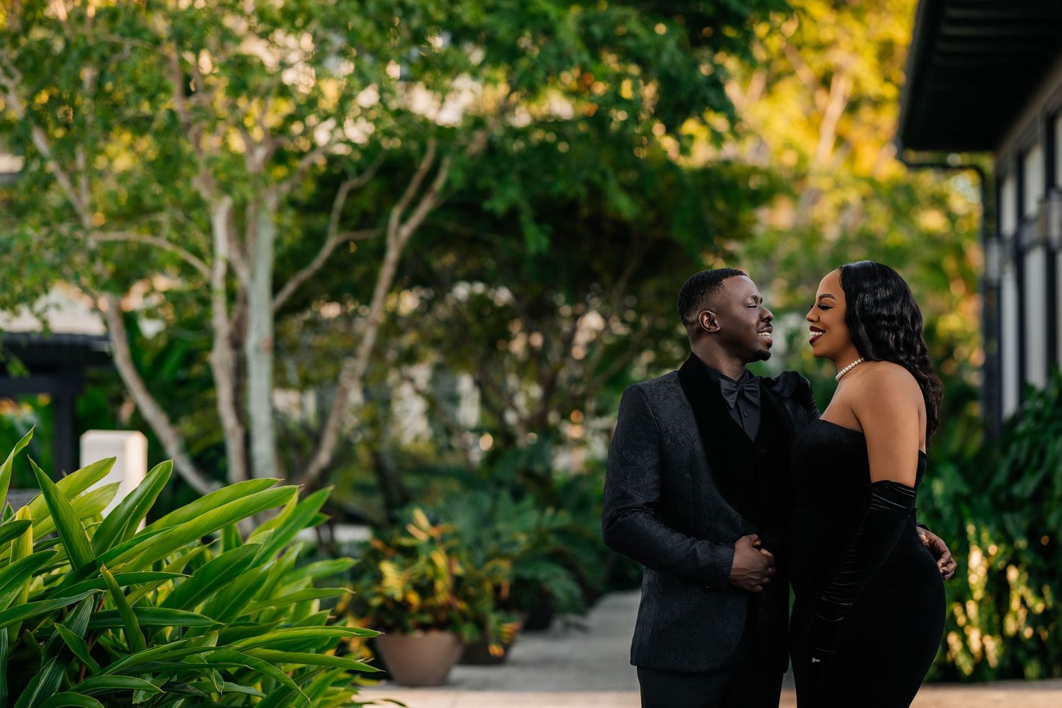 A couple shares a romantic moment at The Island House in a lush garden setting with soft natural lighting and greenery in the background.