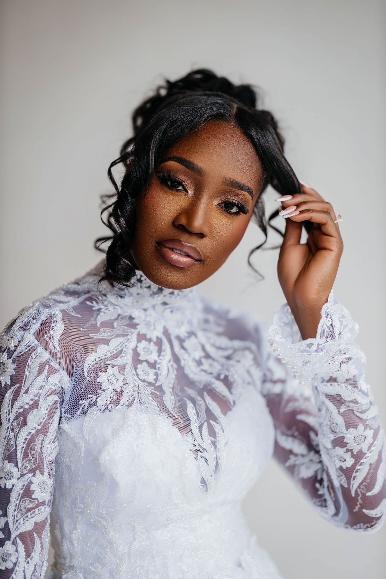 Elegant Black bride in white lace long-sleeve gown with updo hairstyle and glam makeup poses gracefully.