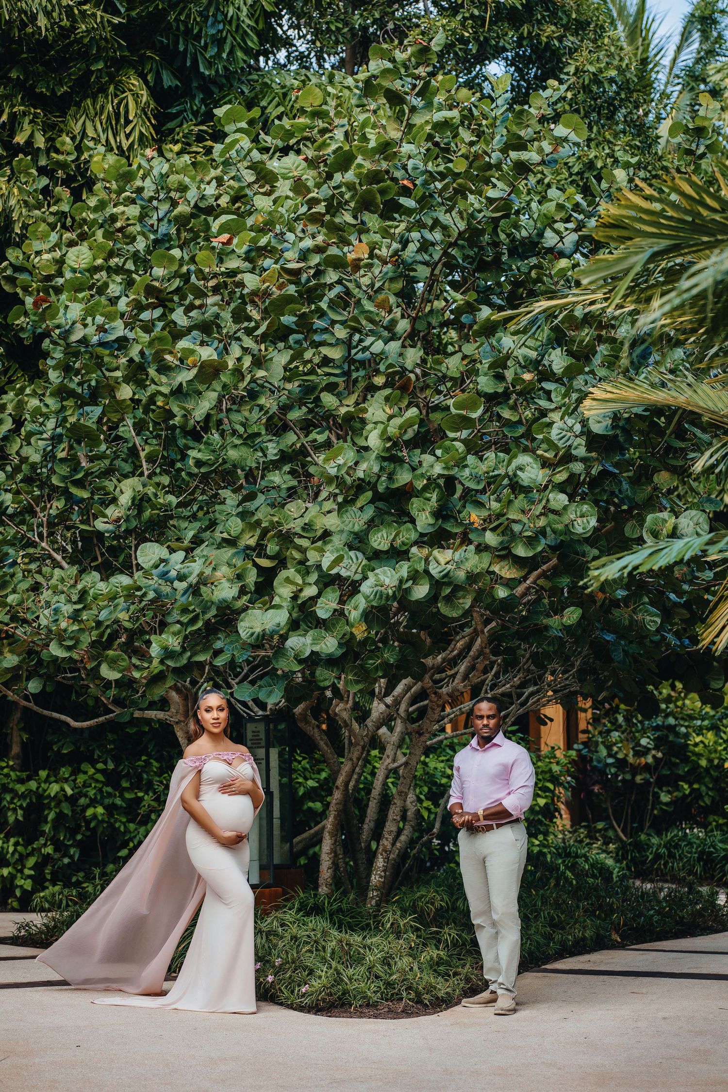 A maternity photo session in a lush garden setting with two figures in elegant attire.