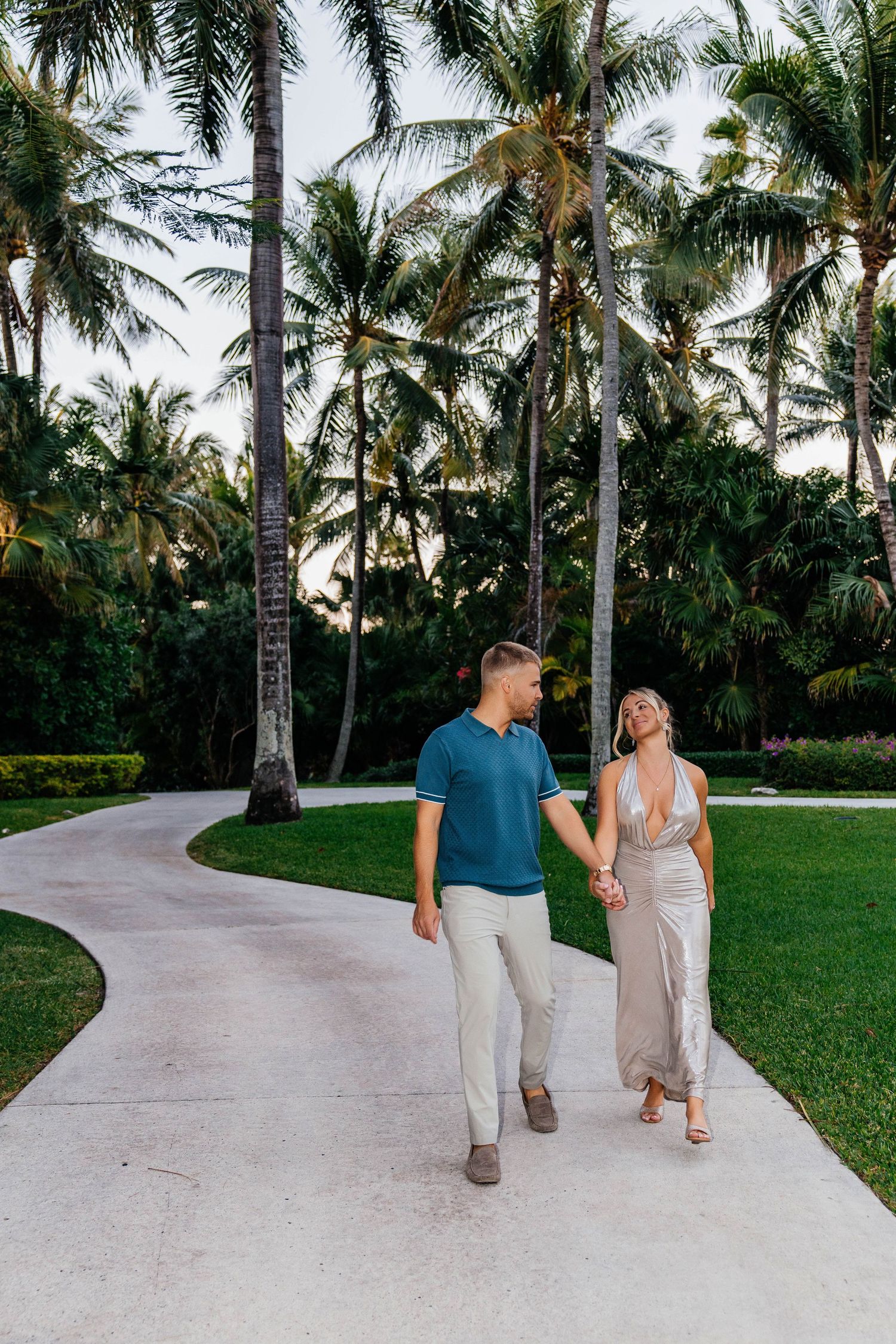 Couple walking hand in hand on pathway surrounded by tropical palm trees.