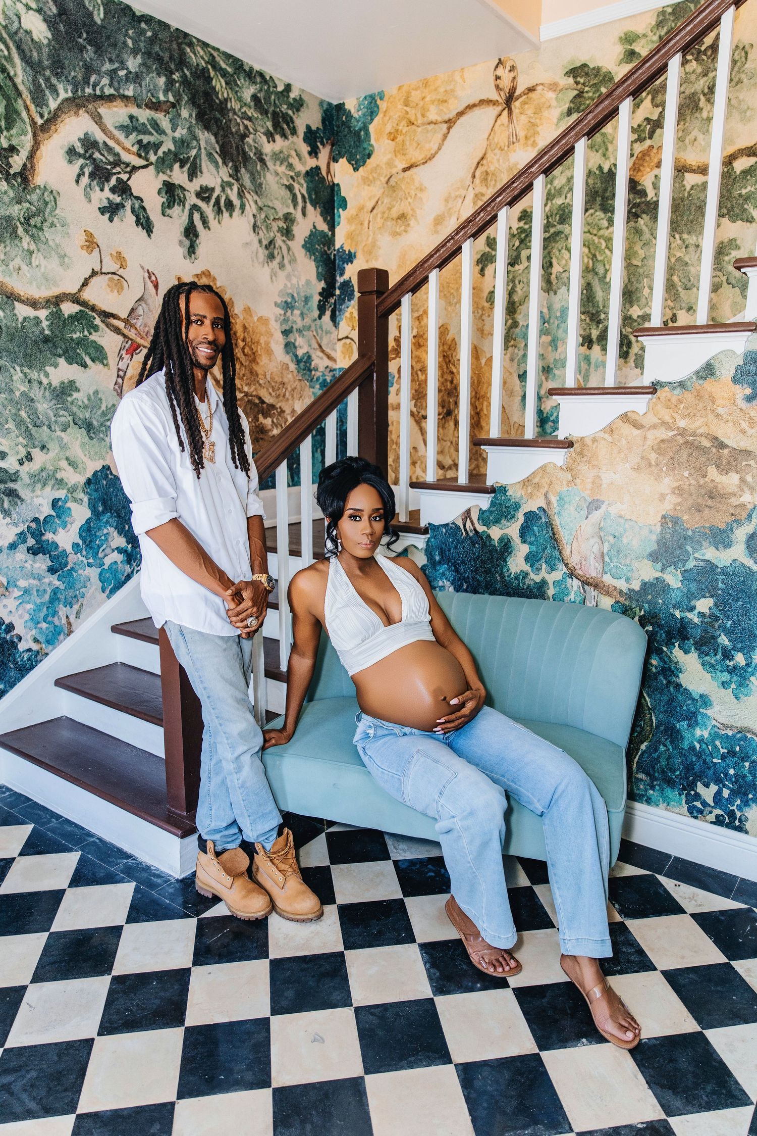 Maternity photoshoot in front of colorful wall mural with a blue couch and checkered floor.