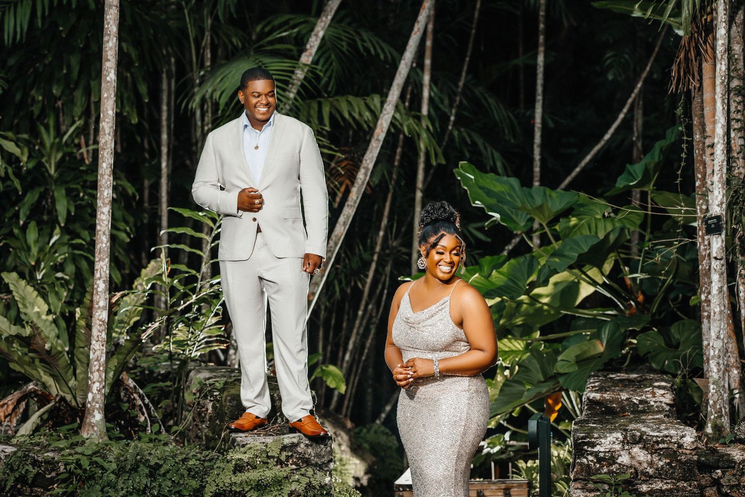 Newlyweds in white attire pose separately on tropical forest steps.