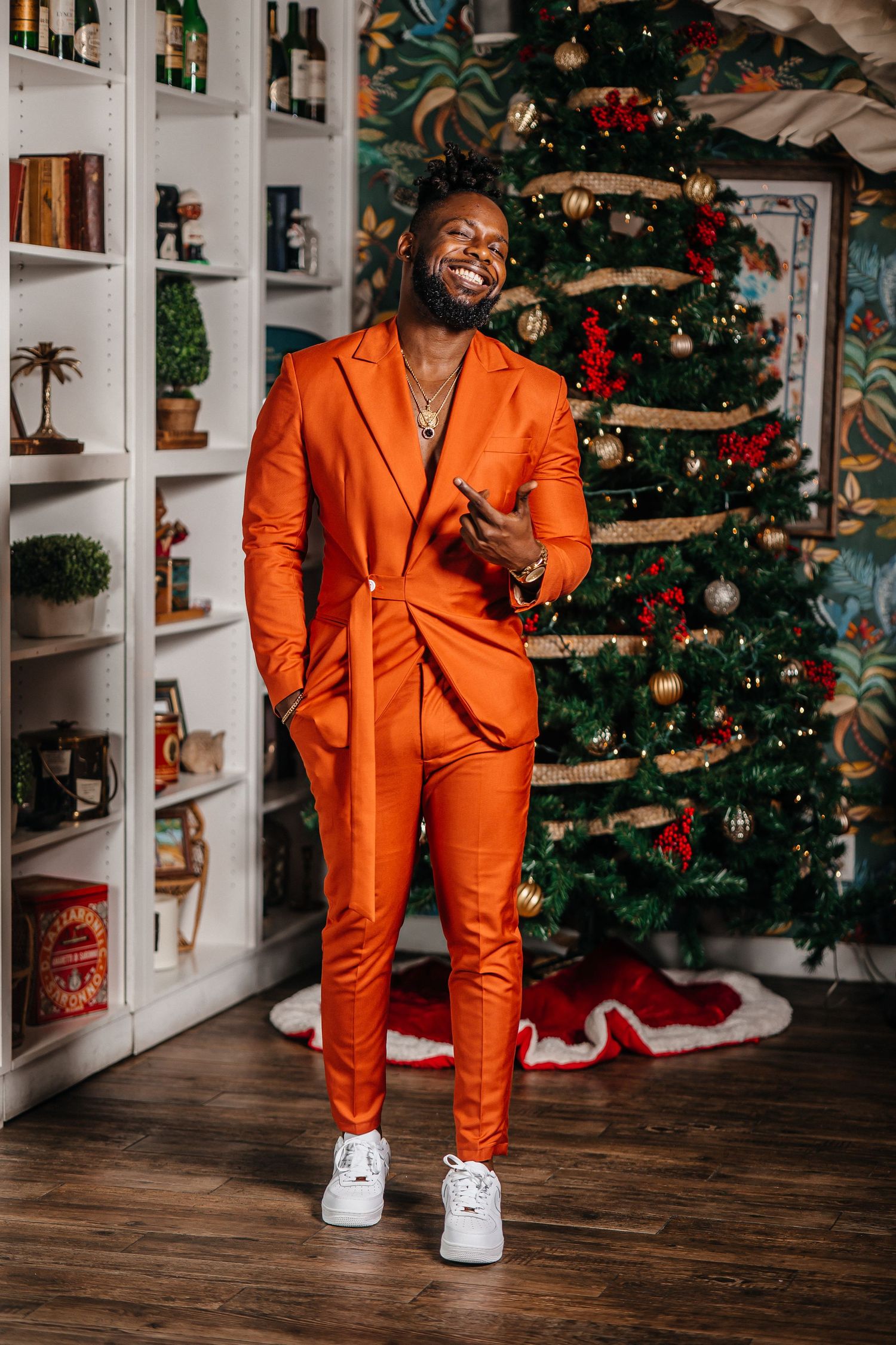 Bright orange suit creates festive contrast against decorated Christmas tree backdrop in modern setting.