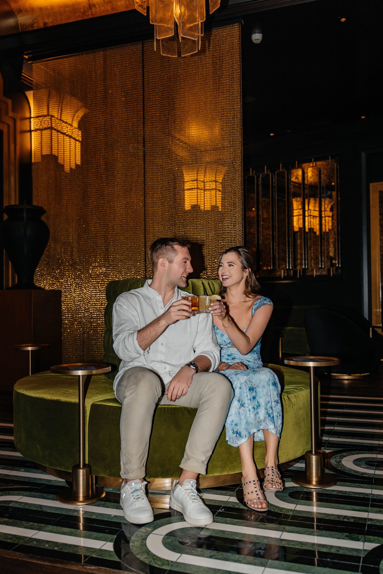 A couple sharing drinks and conversation in an elegantly lit lounge setting.