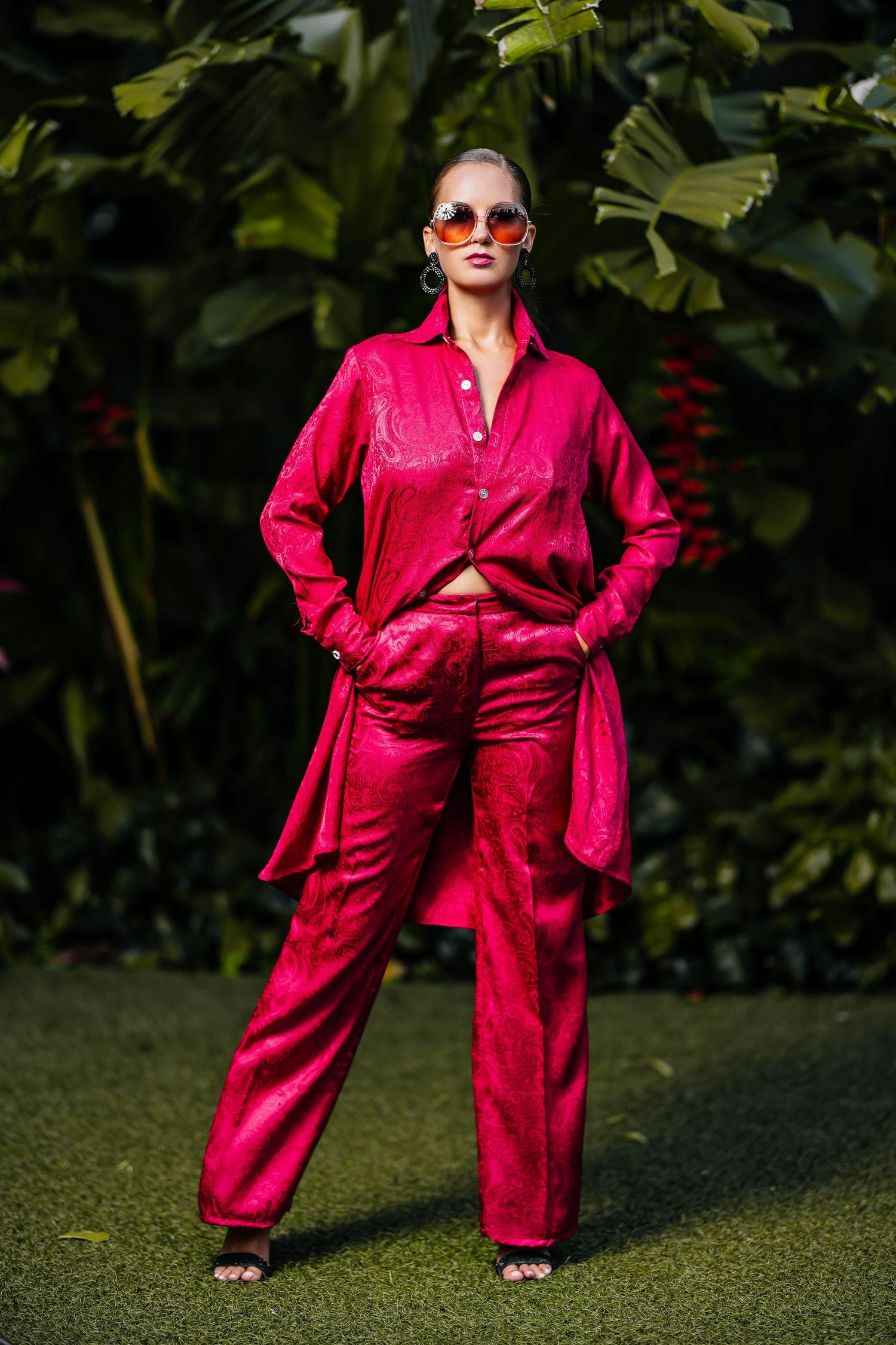Bold red silk pantsuit with matching blazer styled against tropical garden setting.