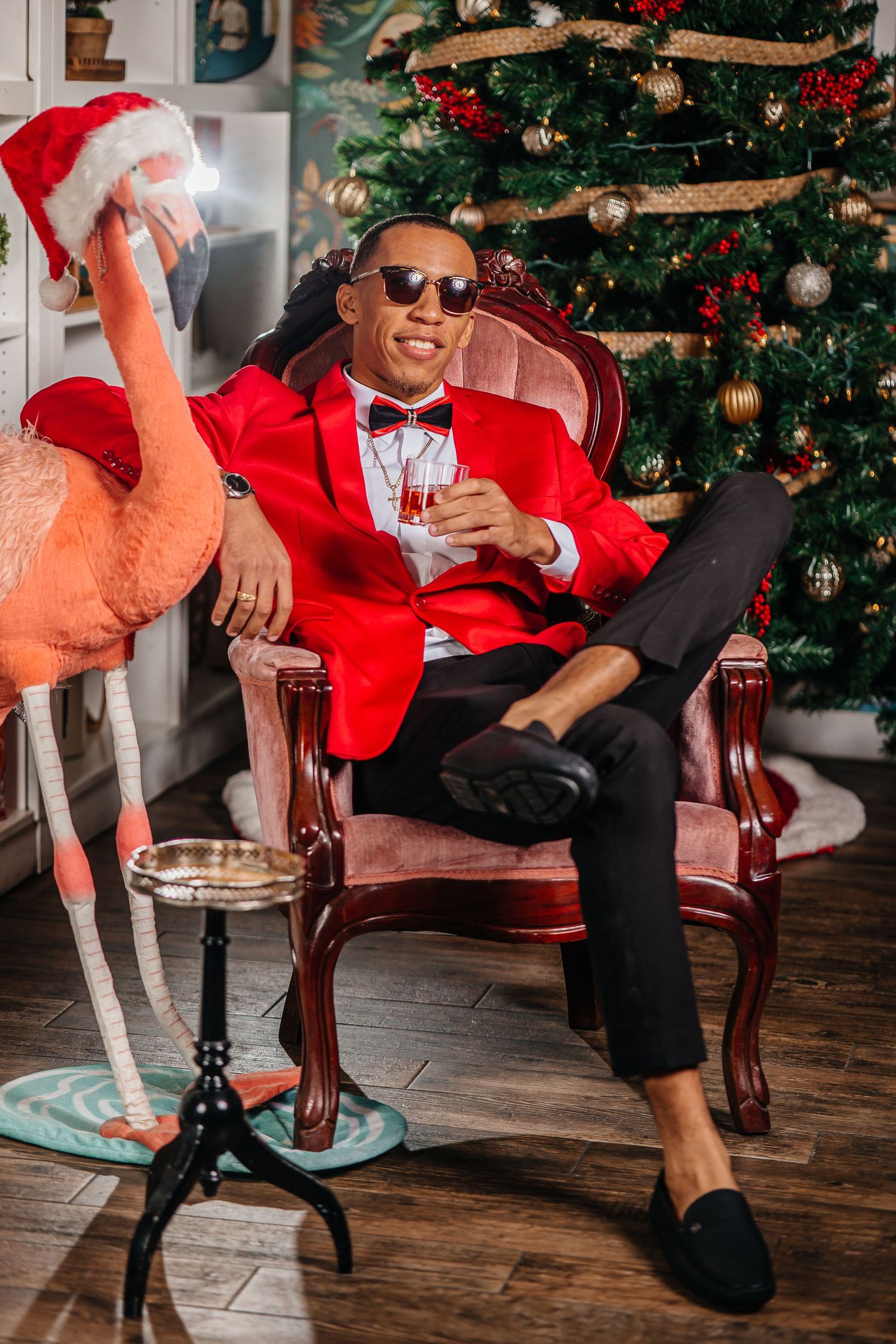 Festive red suit and bow tie holiday portrait with flamingo decoration by Christmas tree.