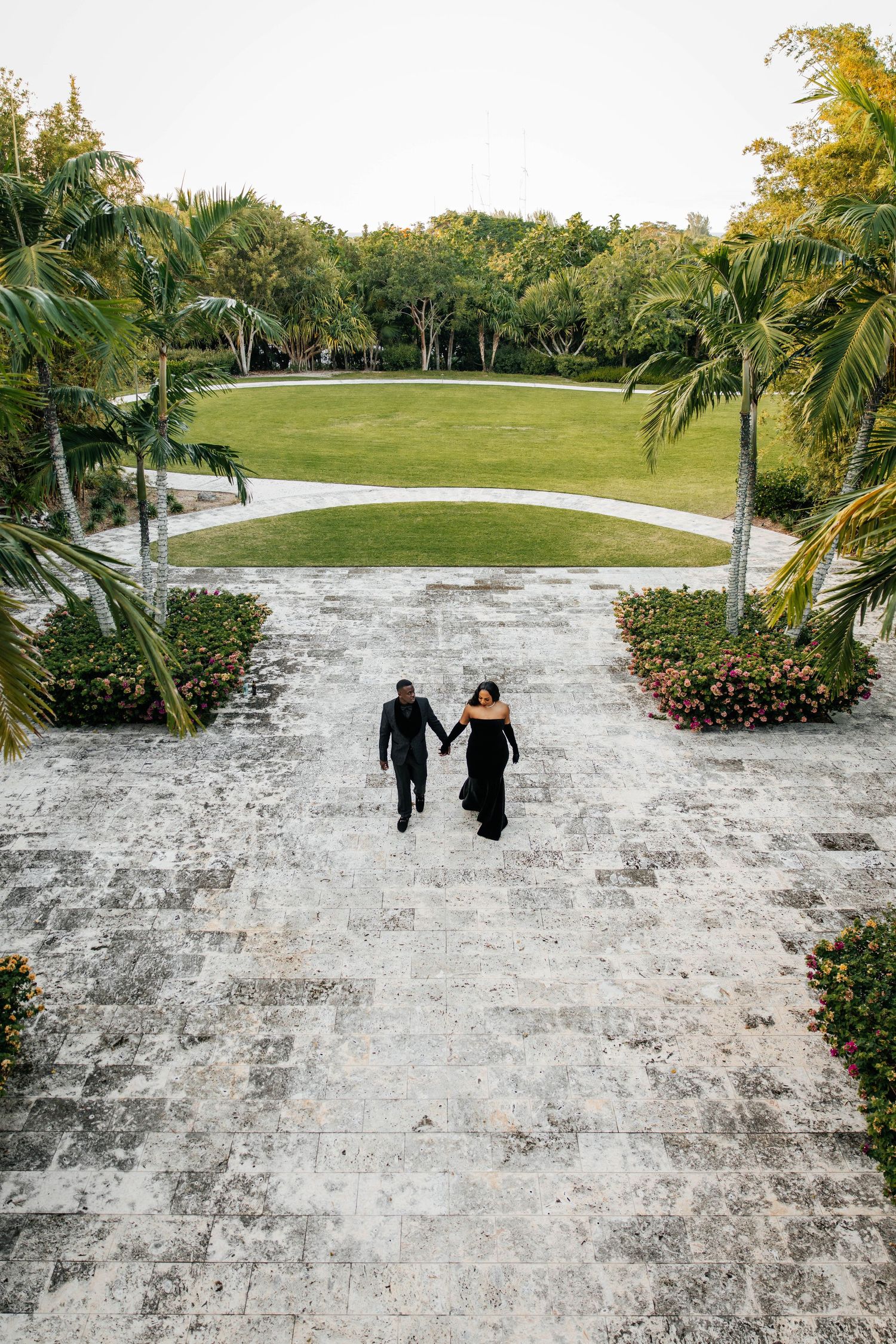 A snowy white pathway leads through a lush tropical garden with palm trees and green landscaping.