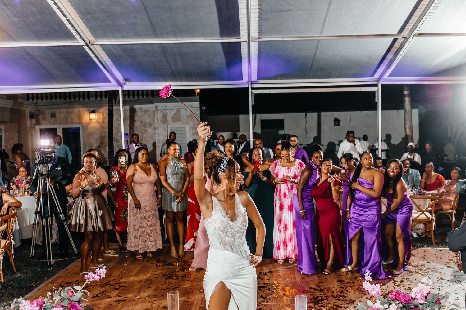 Bride tossing bouquet to excited guests in colorful dresses at elegant wedding reception.