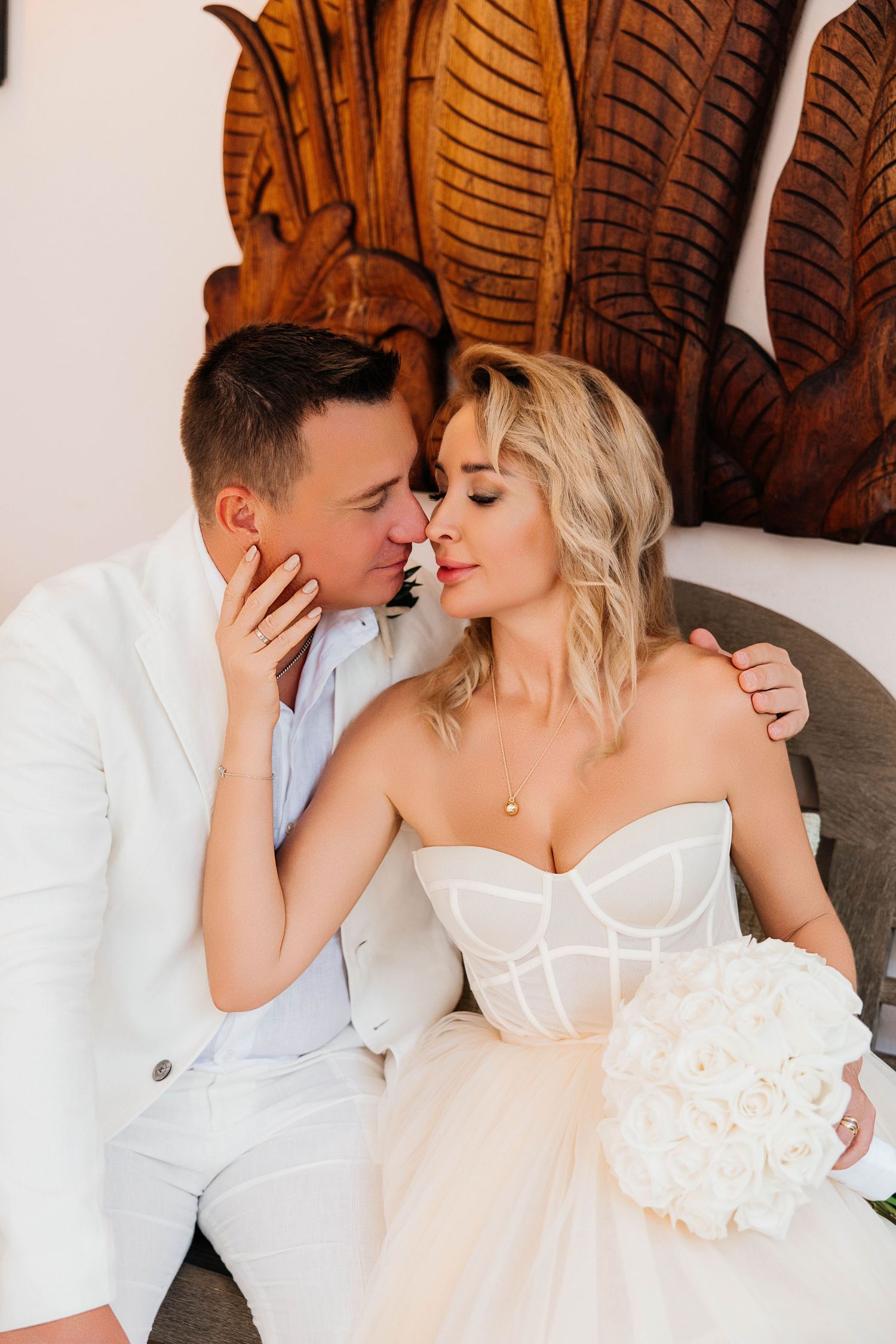 A tender moment between newlyweds against an ornate wooden backdrop with white roses.
