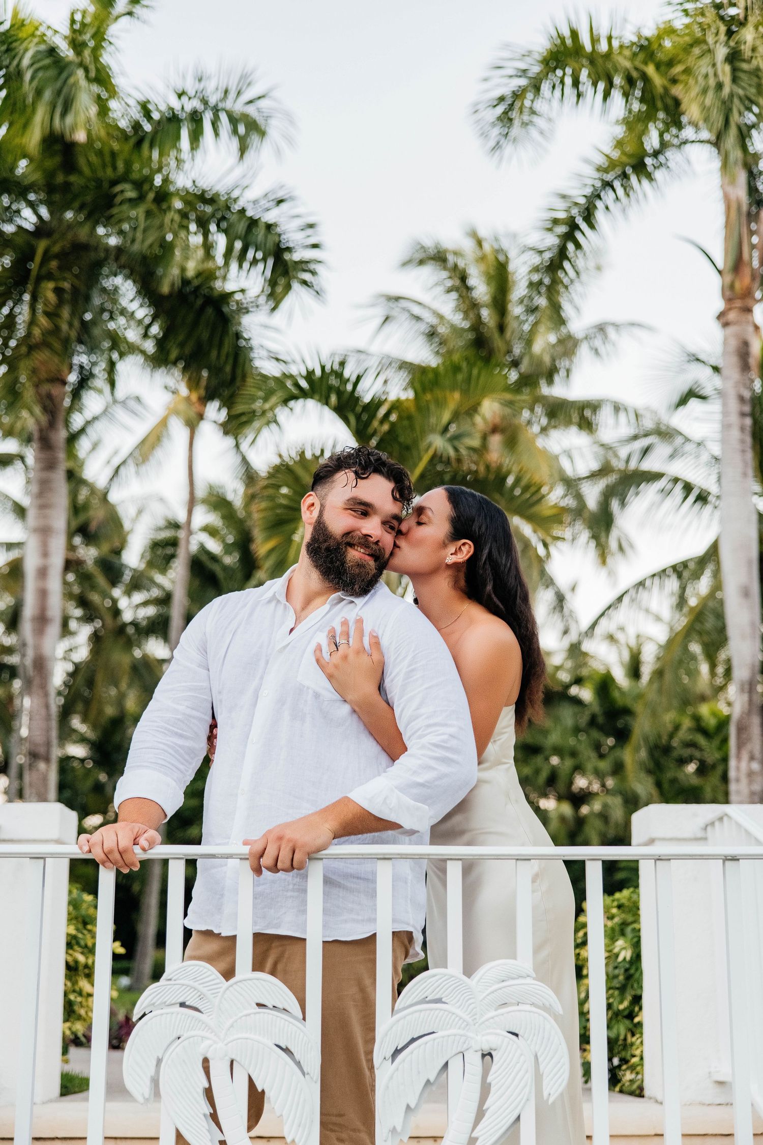 A couple shares a romantic moment on a tropical balcony with palm leaf decorations.