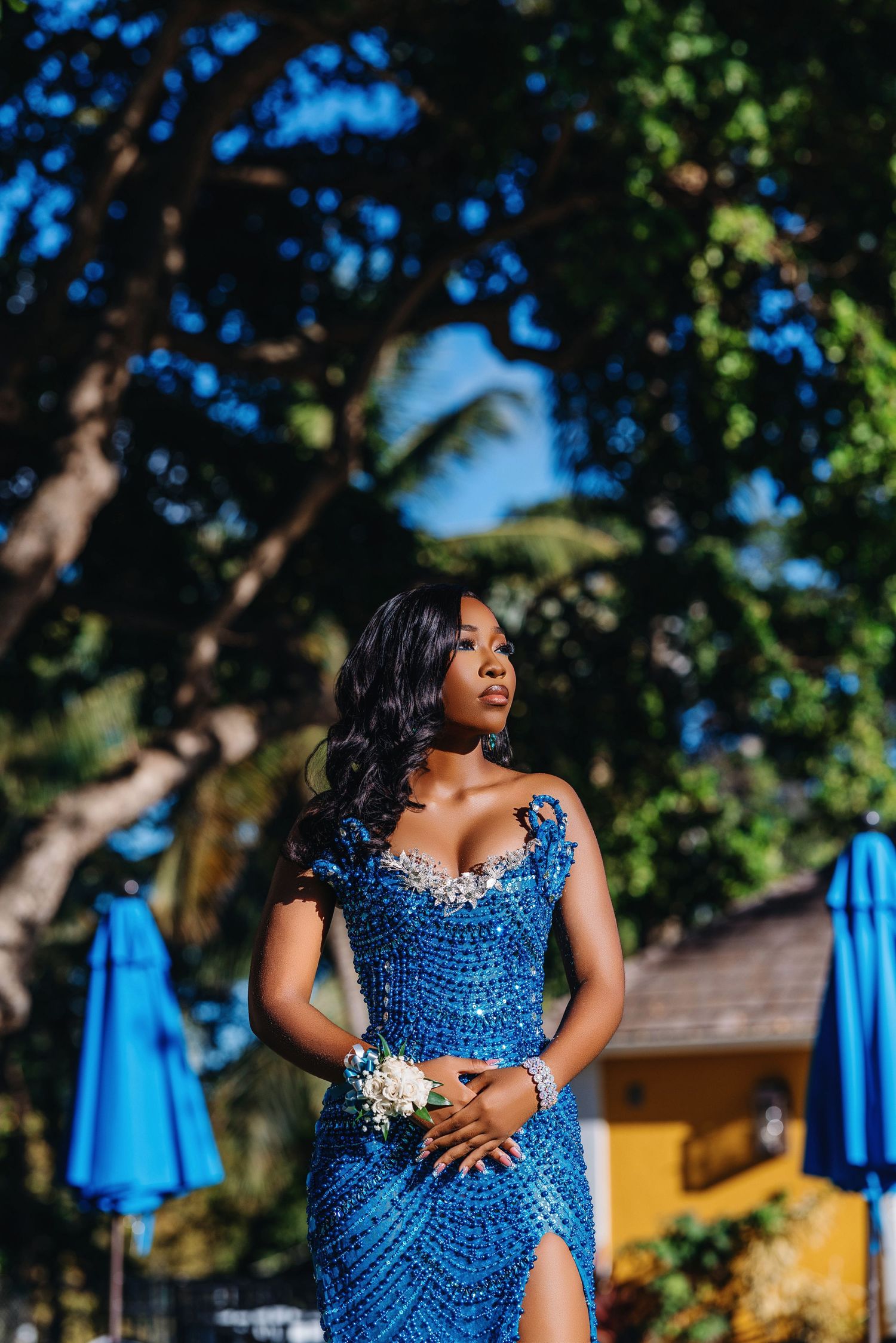 Elegant figure in a sparkling blue sequined dress poses outdoors with baby's breath flowers against a sunny garden backdrop.