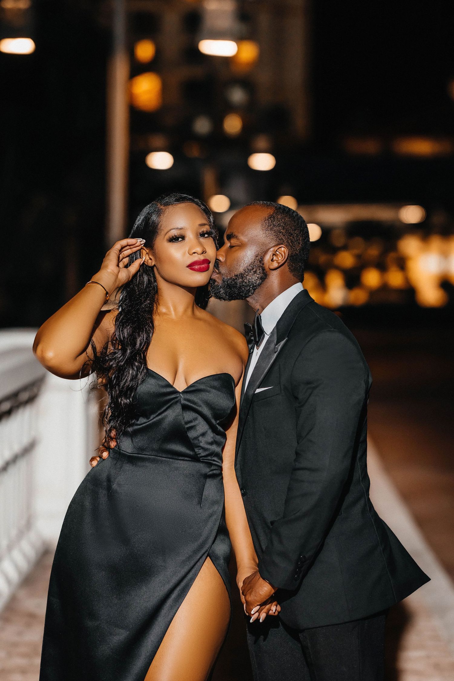 Romantic couple in evening wear share intimate moment on outdoor terrace.