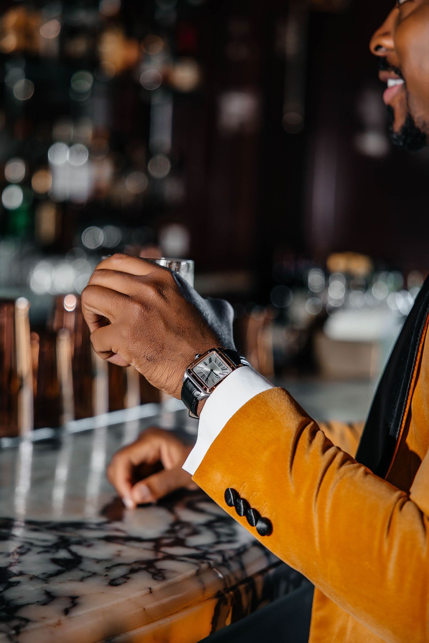 Person in yellow blazer checking stylish watch while sitting at marble bar counter.