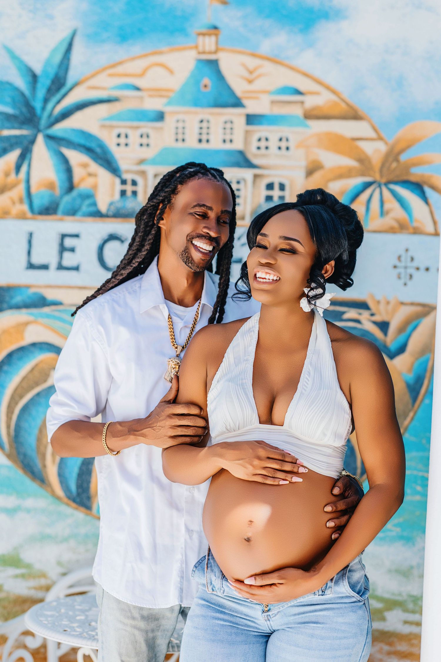 Joyful maternity photo in front of tropical mural with palm trees.