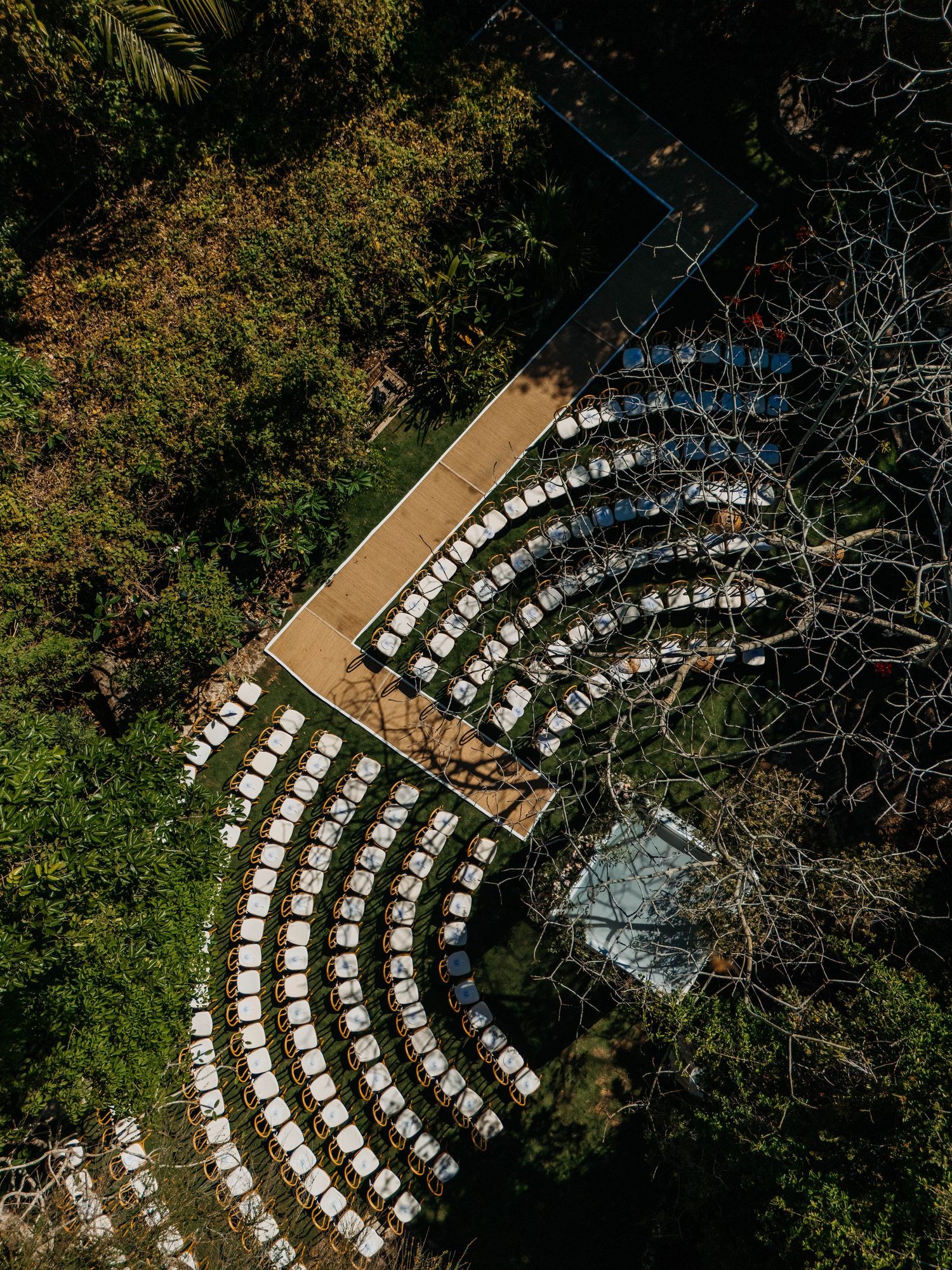 Aerial view of curved rows of white chairs arranged in semicircle pattern for outdoor wedding ceremony surrounded by lush trees.