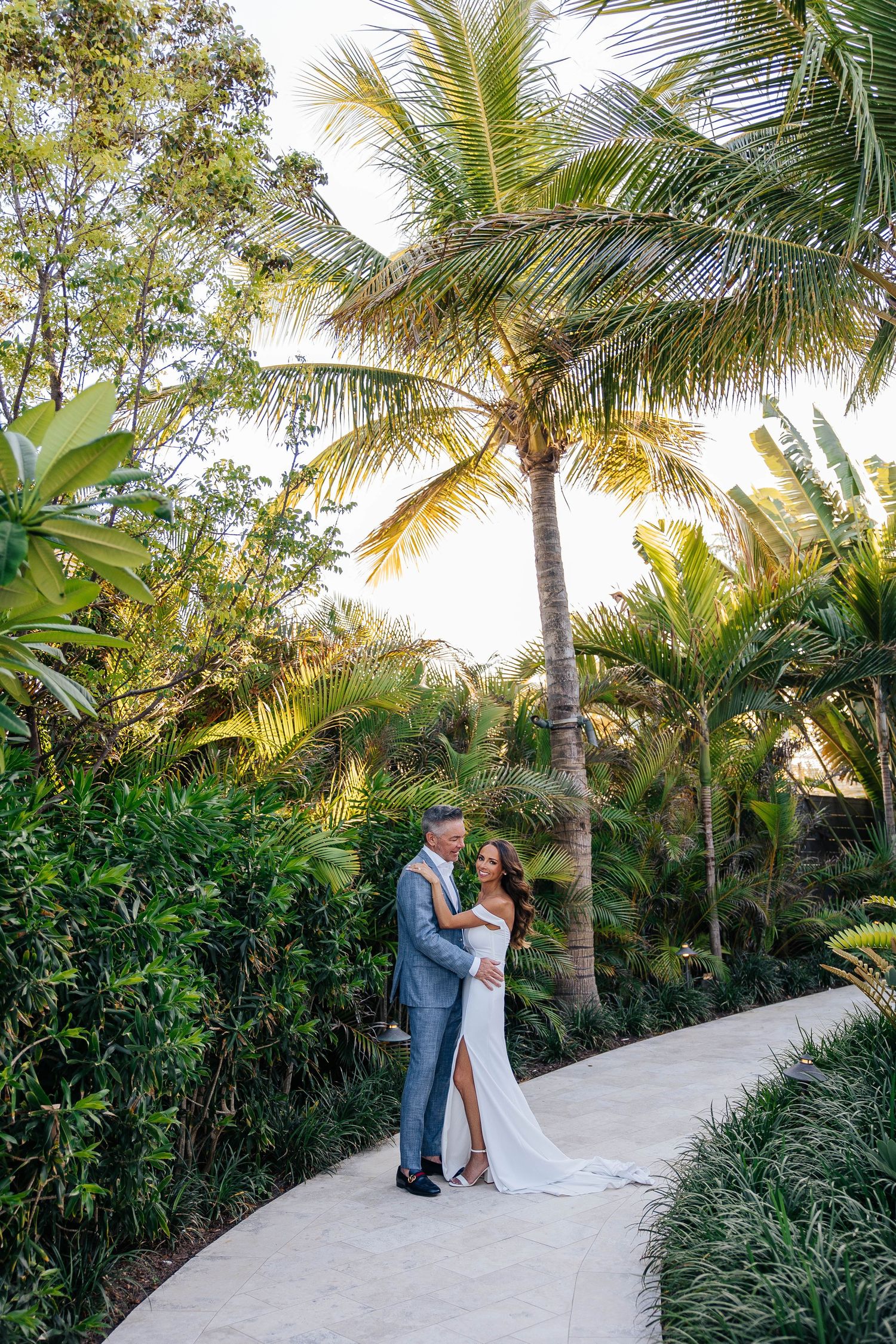 Romantic couple embracing on garden path beneath swaying palm trees.