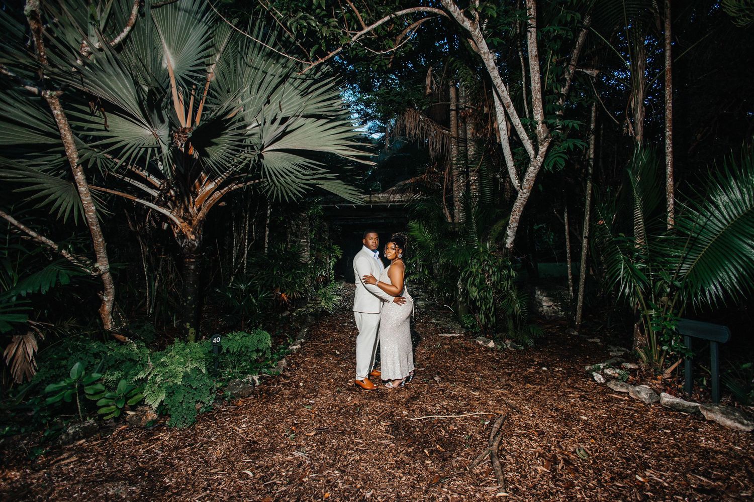 Wedding couple poses on nature trail surrounded by palm trees and foliage.