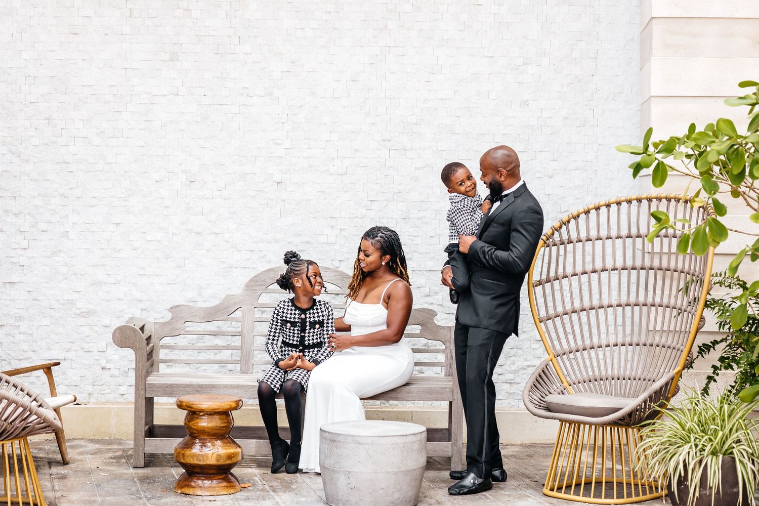 Family gathered on rustic outdoor patio with woven chairs and white wall backdrop.