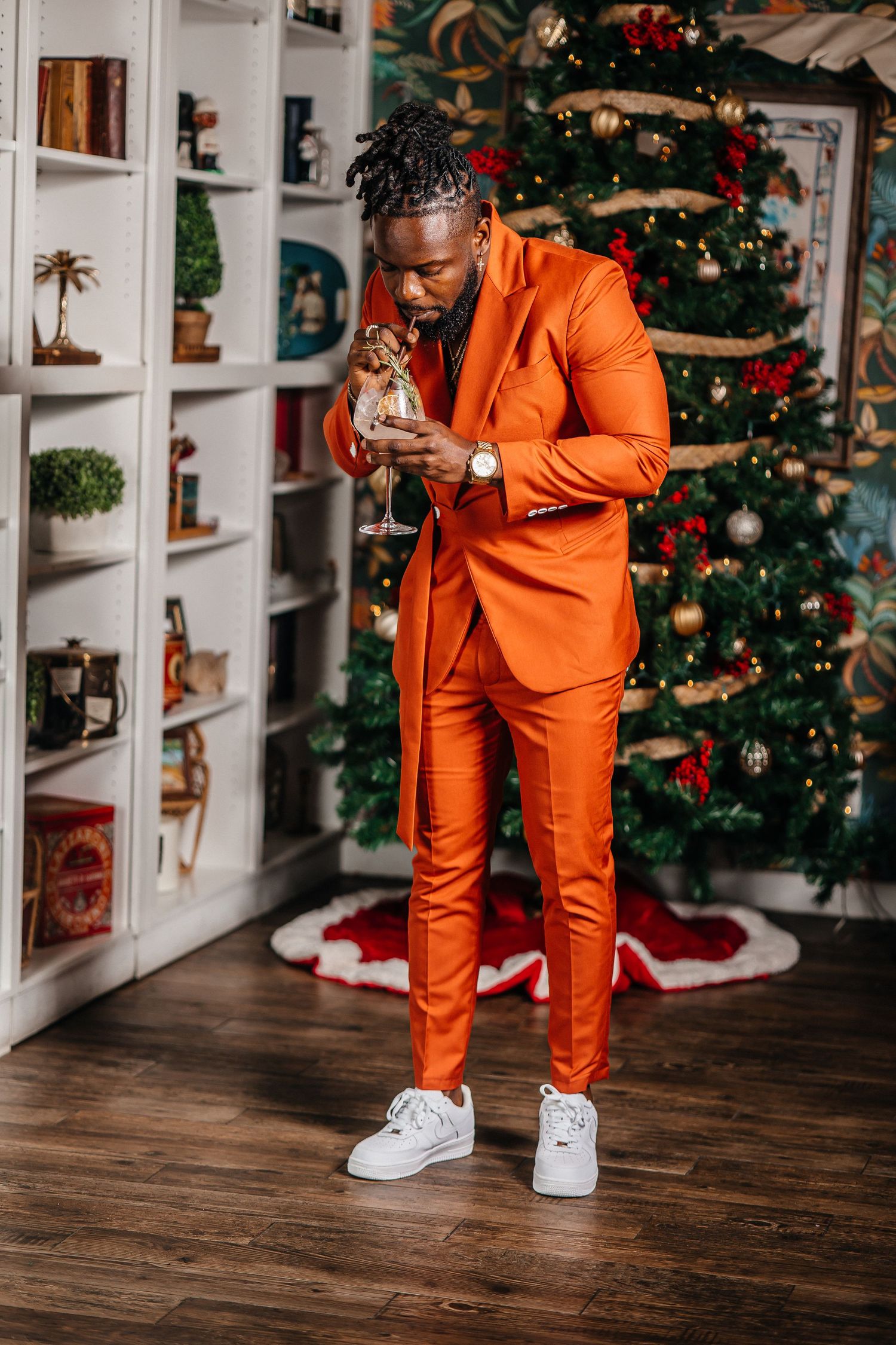 Stylish orange suit paired with white sneakers captured in front of a decorated Christmas tree setting.