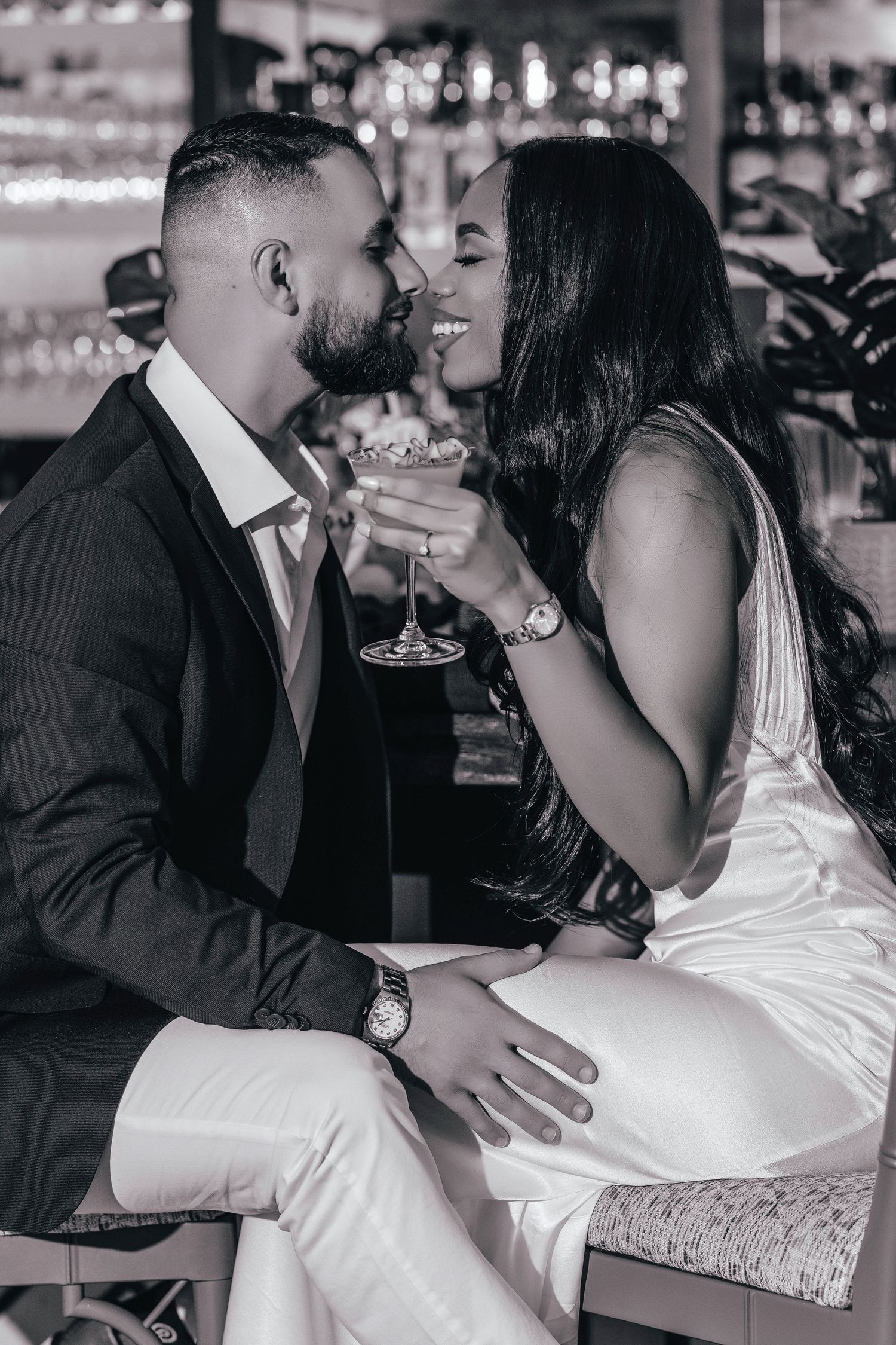 Romantic black and white photo of couple sharing cocktails at elegant bar.