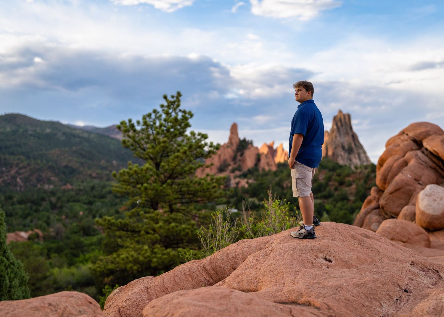 Man standing on red rocks overlooking Garden of the Gods with dramatic spires and mountains in Colorado Springs.