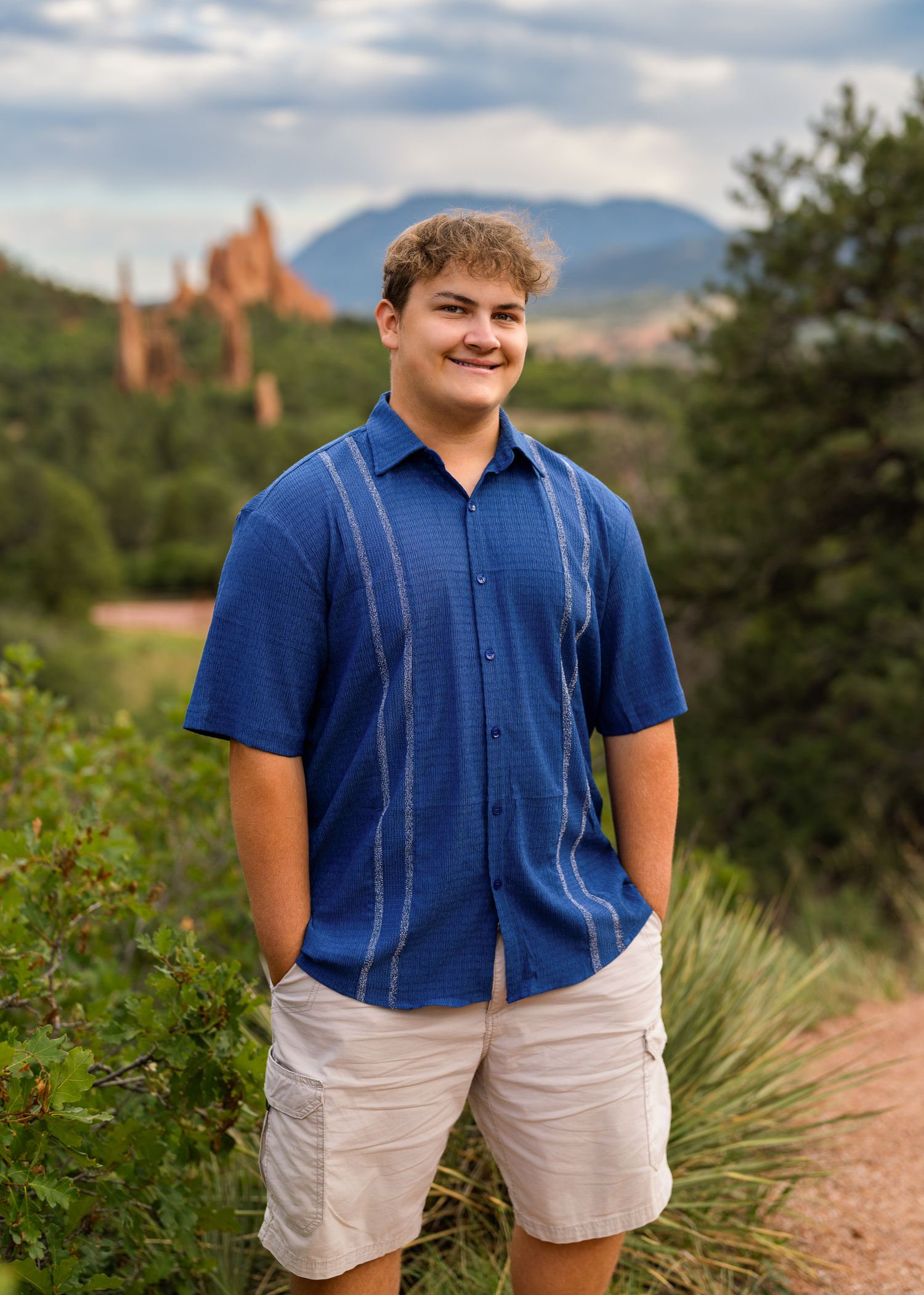 Young man in blue striped shirt and khaki shorts smiling outdoors at Garden of the Gods, Colorado.