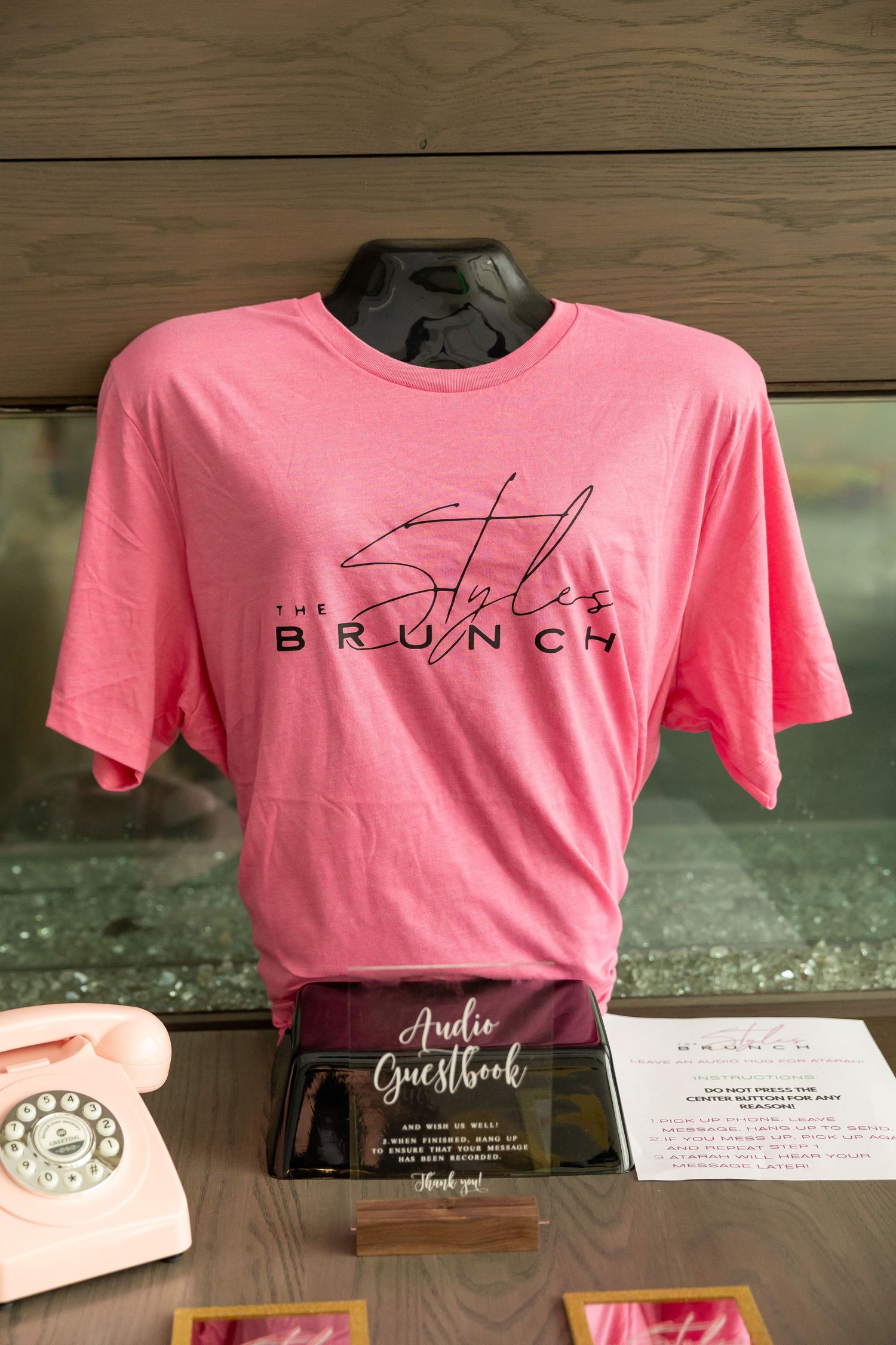 Pink Styles Brunch branded t-shirt displayed on mannequin next to audio guestbook sign and vintage pink phone.