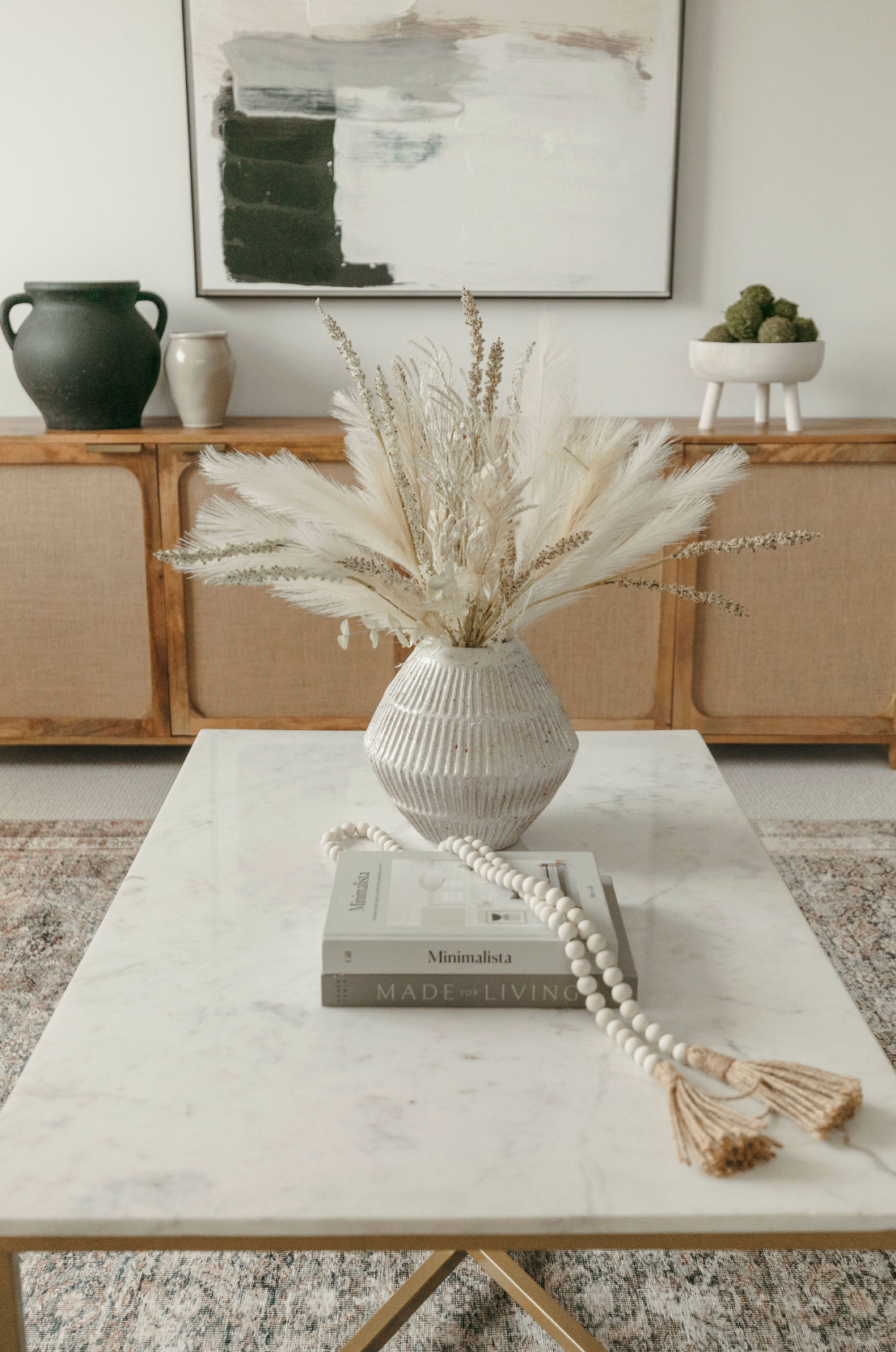 Boho living room coffee table with marble top, dried pampas grass in white vase, books, and rattan sideboard backdrop.