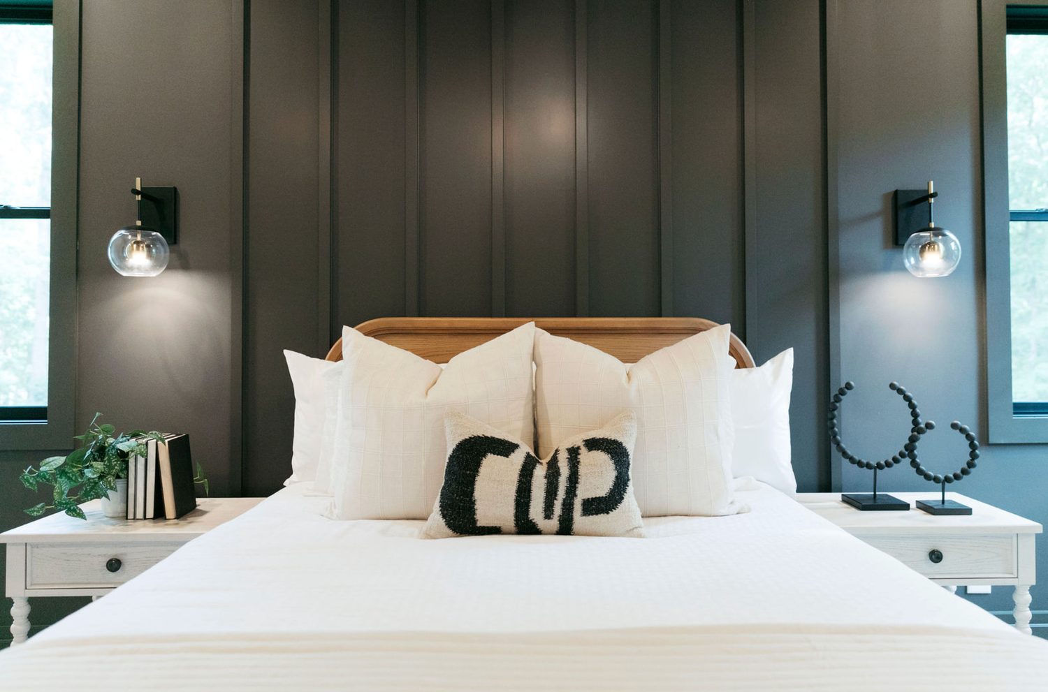 Modern bedroom with dark paneled wall, white bedding, decorative pillows, and matching wall sconces on white nightstands.