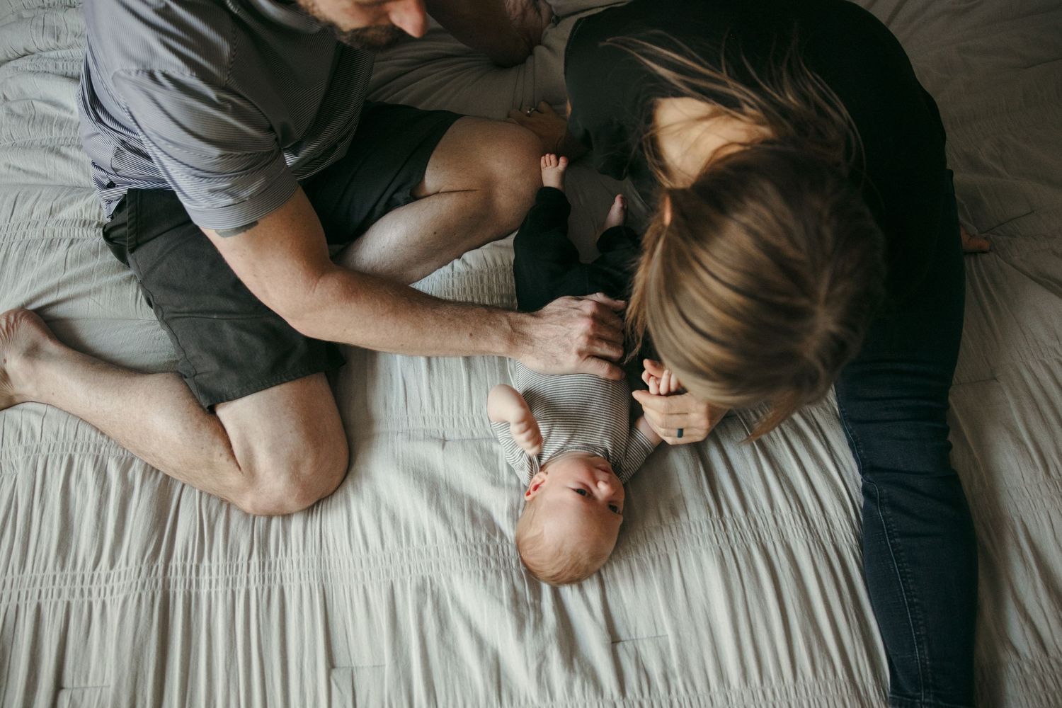 Intimate family photography session captures tender moments on white bedding.