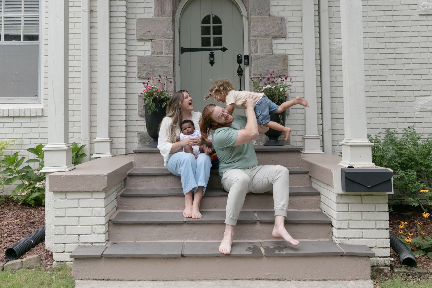 A group sits together on the front steps of a white brick house with a decorative arched doorway.
