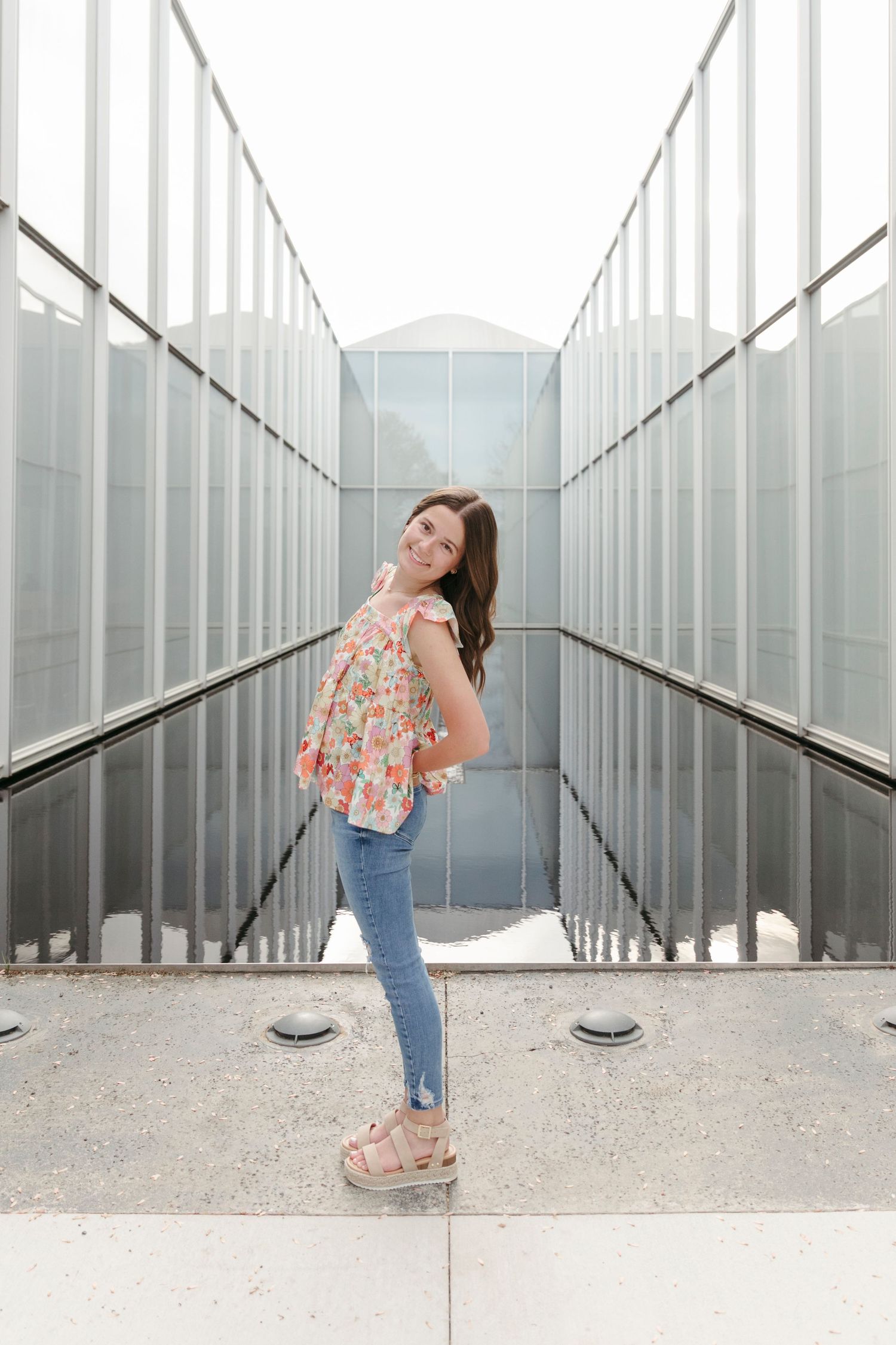 A series of artistic portraits showing person in floral top and jeans posing playfully against modern architectural columns.