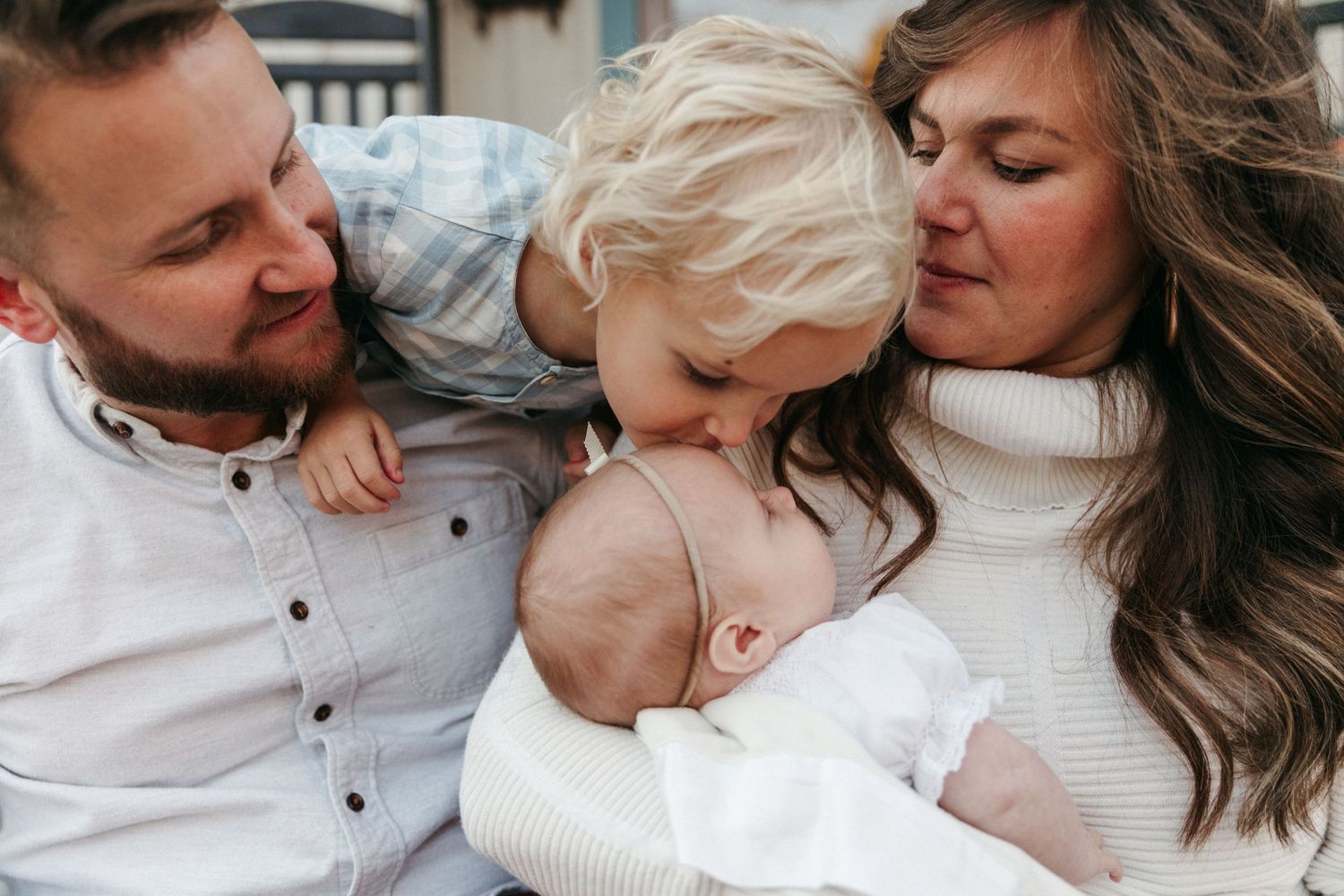 An intimate family moment captured in soft white tones against a light background.