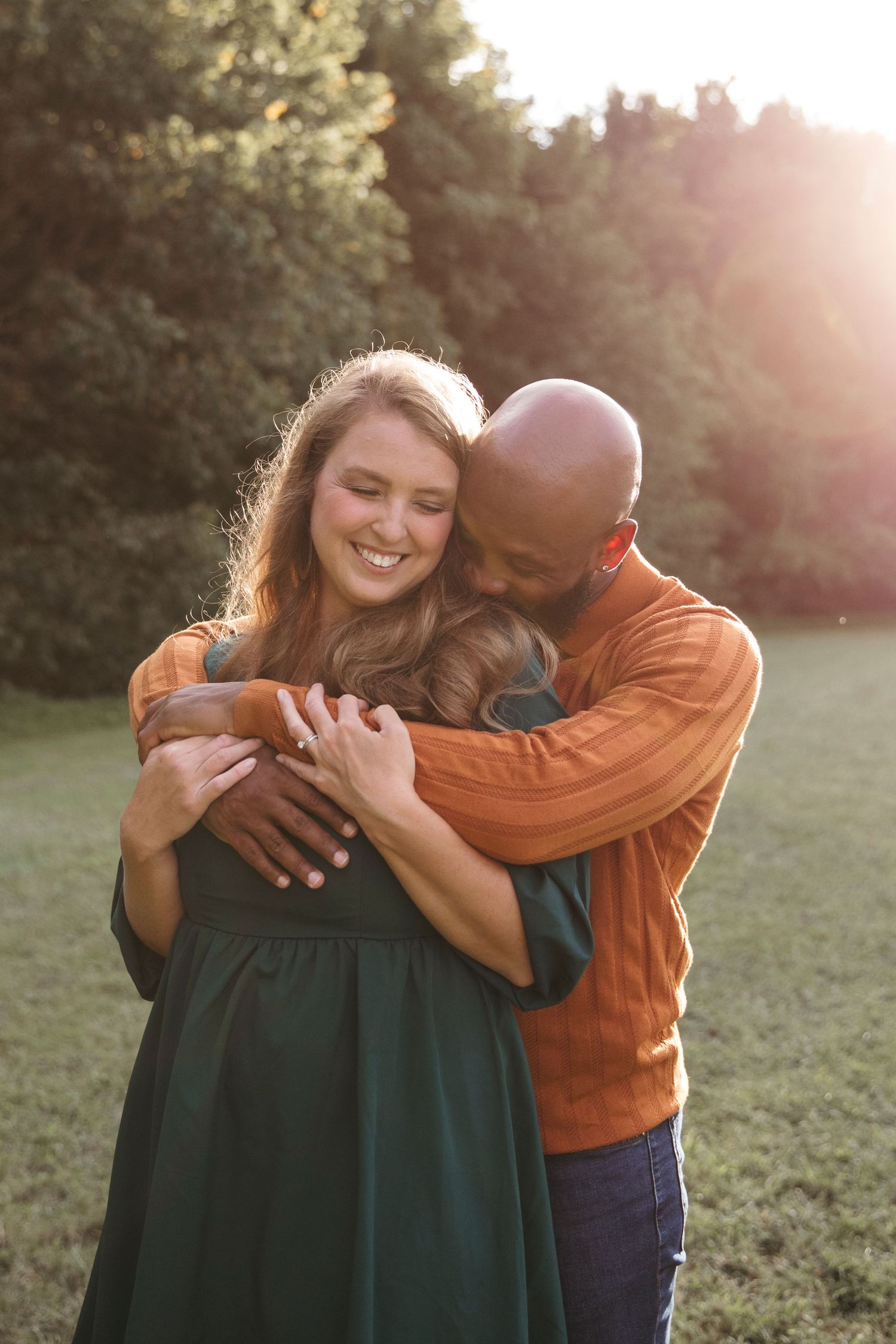 A romantic couple embraces in soft golden sunlight while standing in a peaceful meadow.