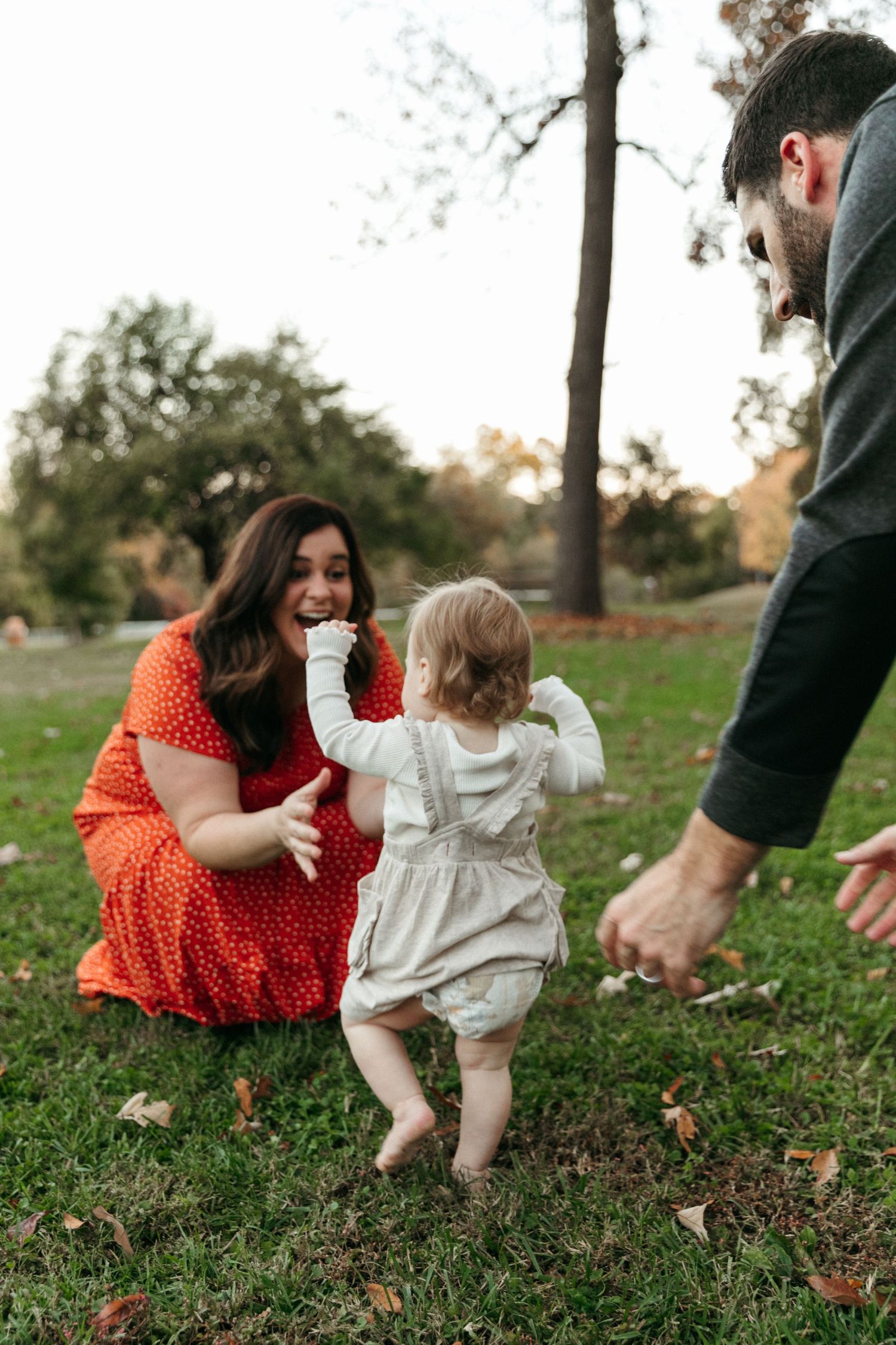 Family playing together on grass with toddler in white outfit.
