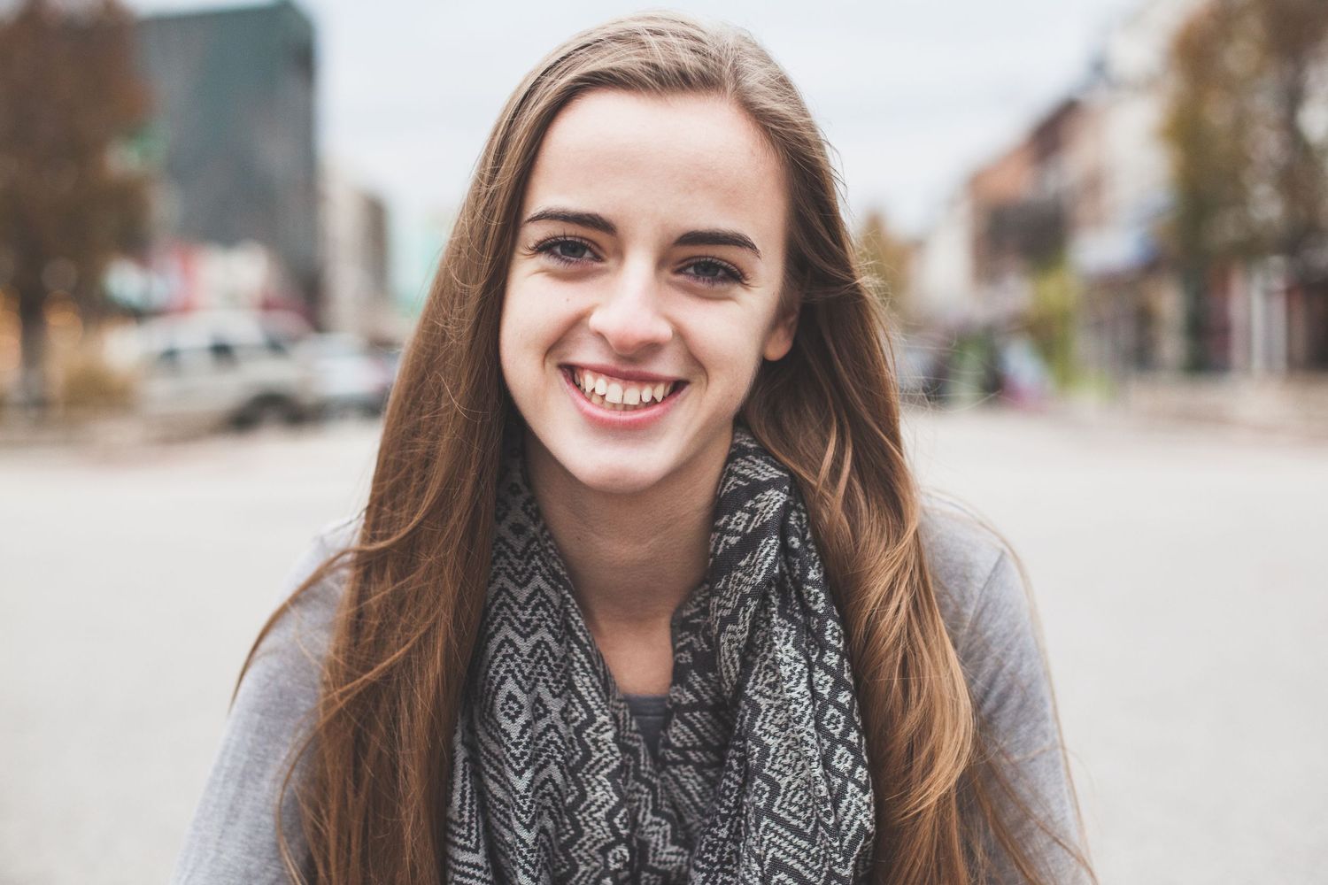 Person with gray scarf smiles warmly during outdoor portrait session.