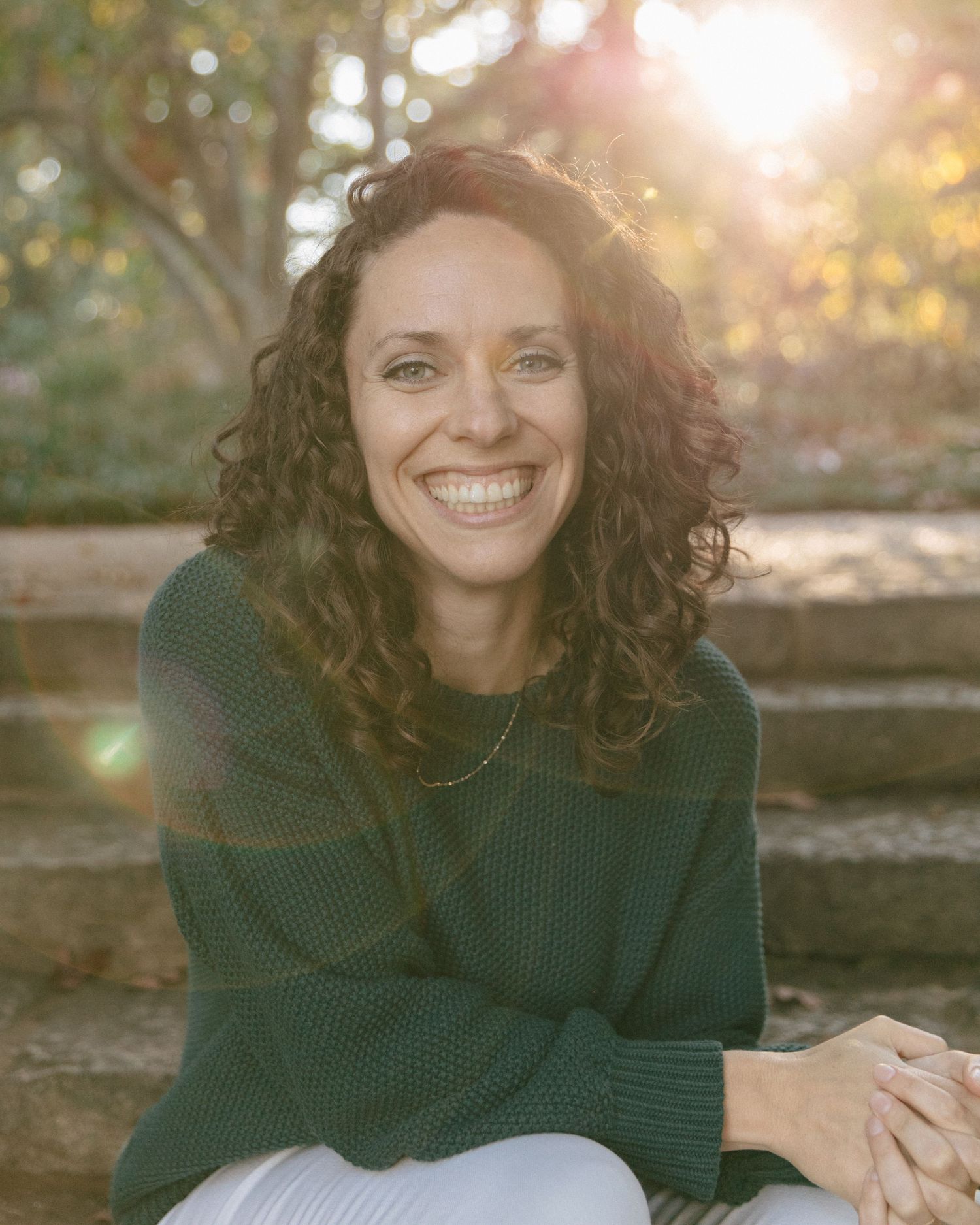 Natural outdoor portraits at sunset featuring someone in an emerald sweater sitting on stone steps.